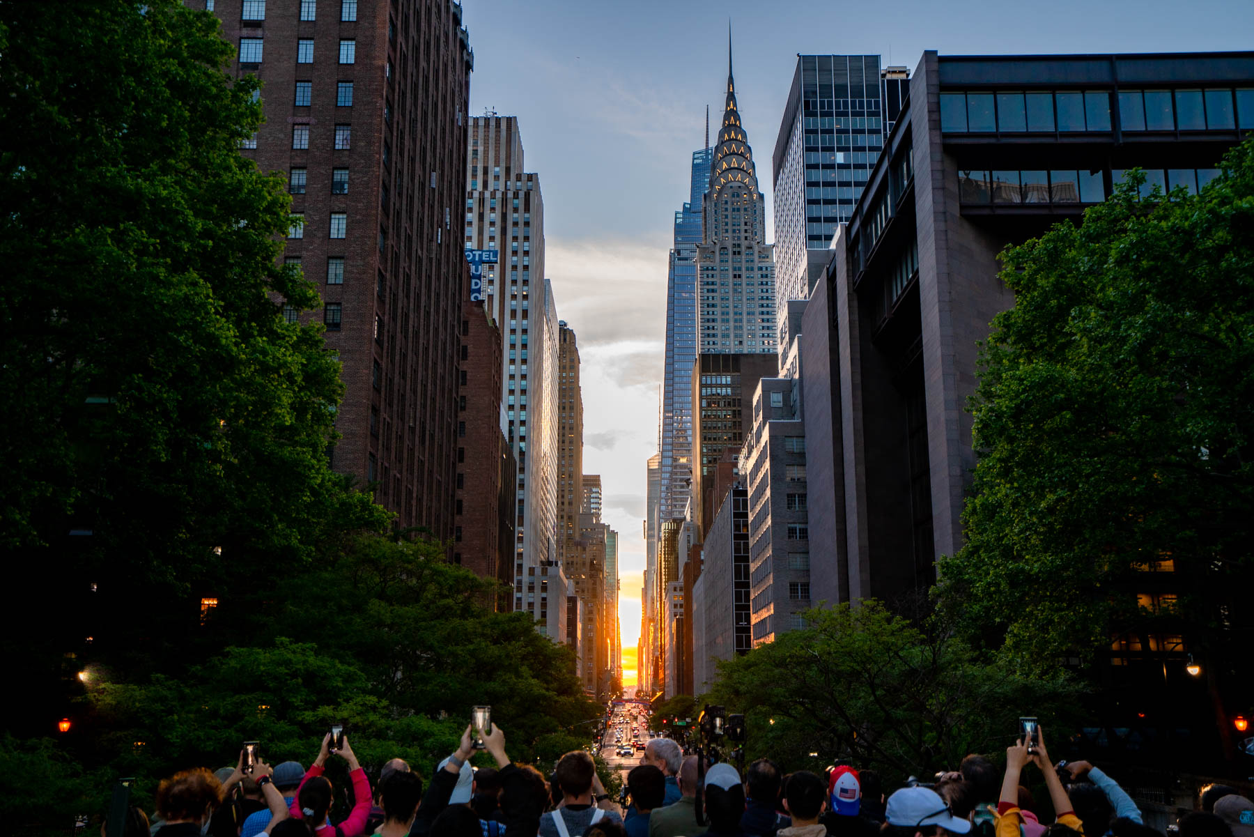 A crowd photographs the Manhattanhenge sunset aligning with 42nd Street and the Chrysler Building.