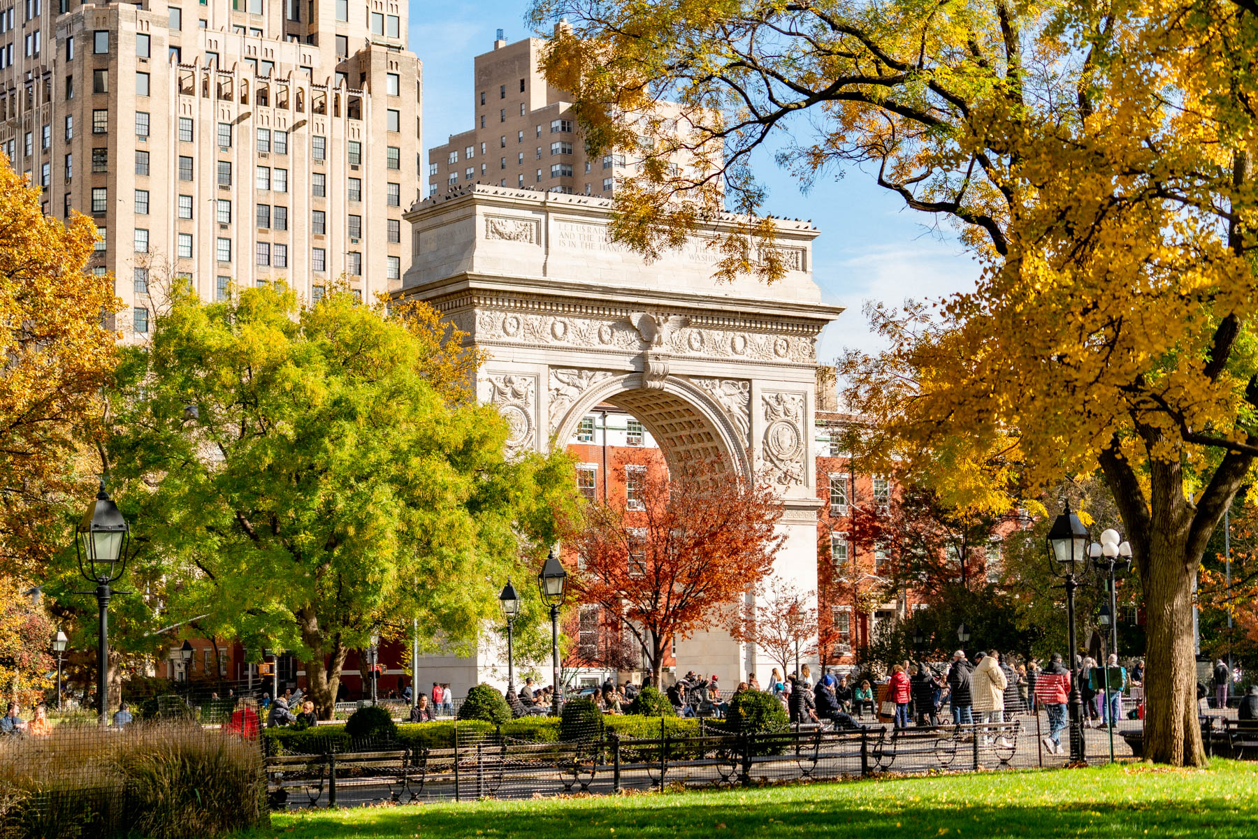 Washington Square Arch is framed by autumn foliage with park visitors below.