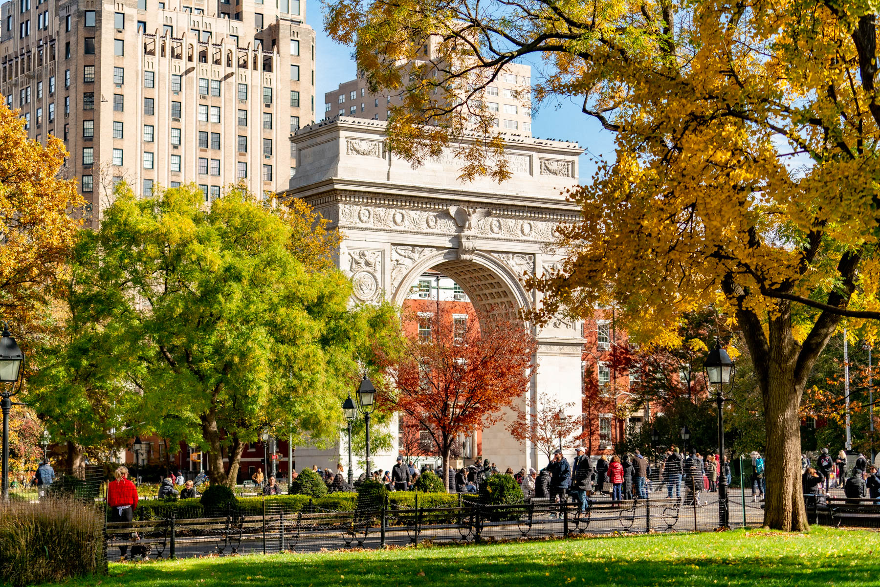 Washington Square Arch stands framed by fall foliage with crowds gathered in the park below.