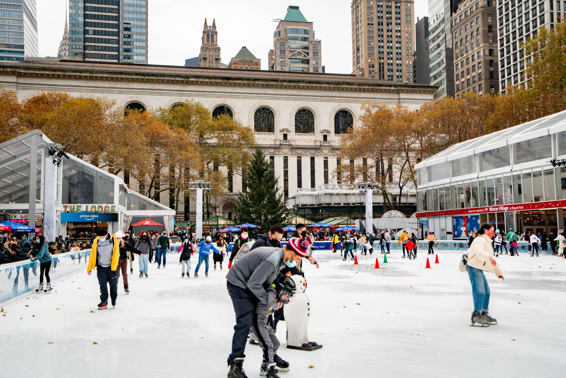 People ice skate at the Bryant Park Winter Village rink with the New York Public Library in the background.