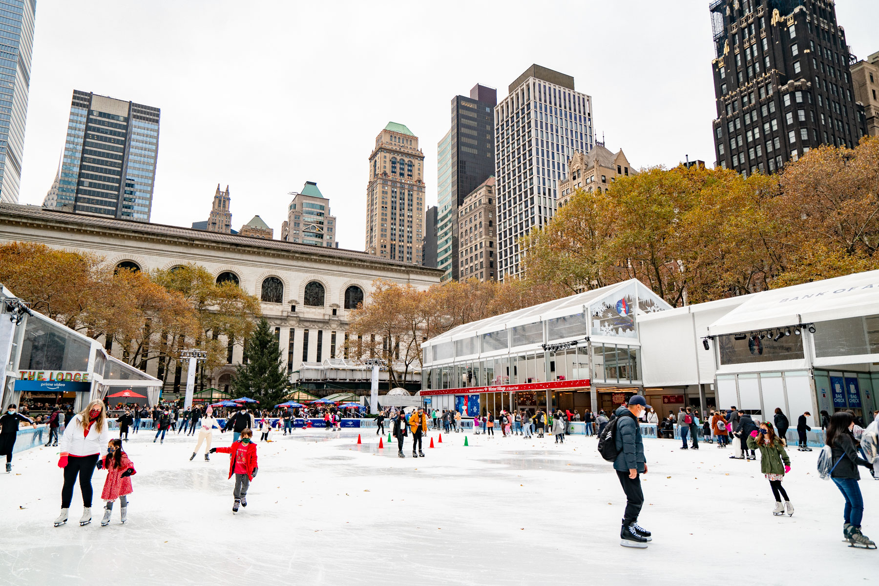 People ice skate at the Bryant Park Winter Village rink surrounded by the city skyline.