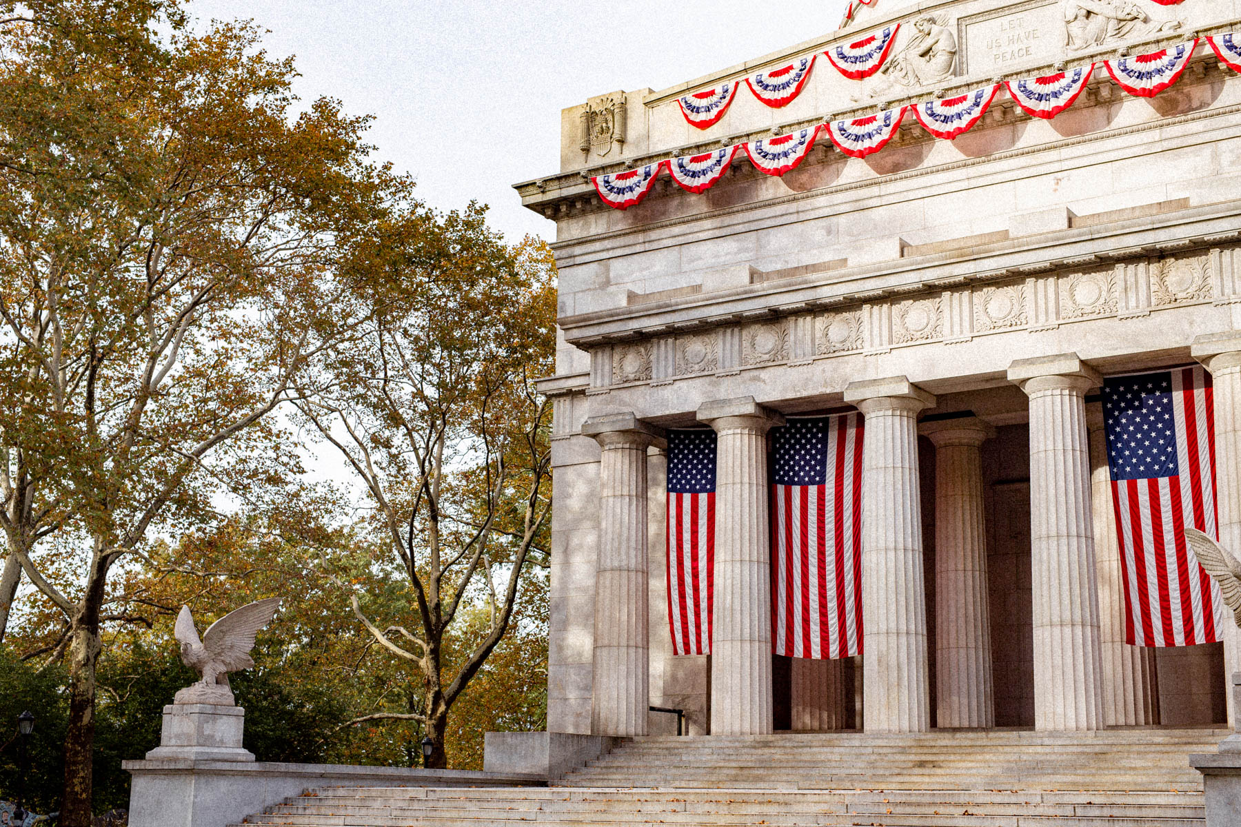 American flags hang between the columns of Grant's Tomb with patriotic bunting above.