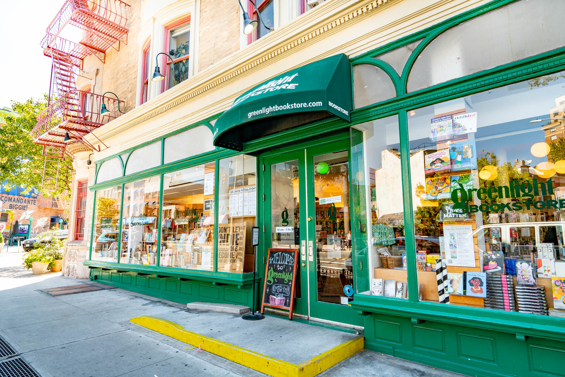 The green storefront of Greenlight Bookstore on a sunny street corner.