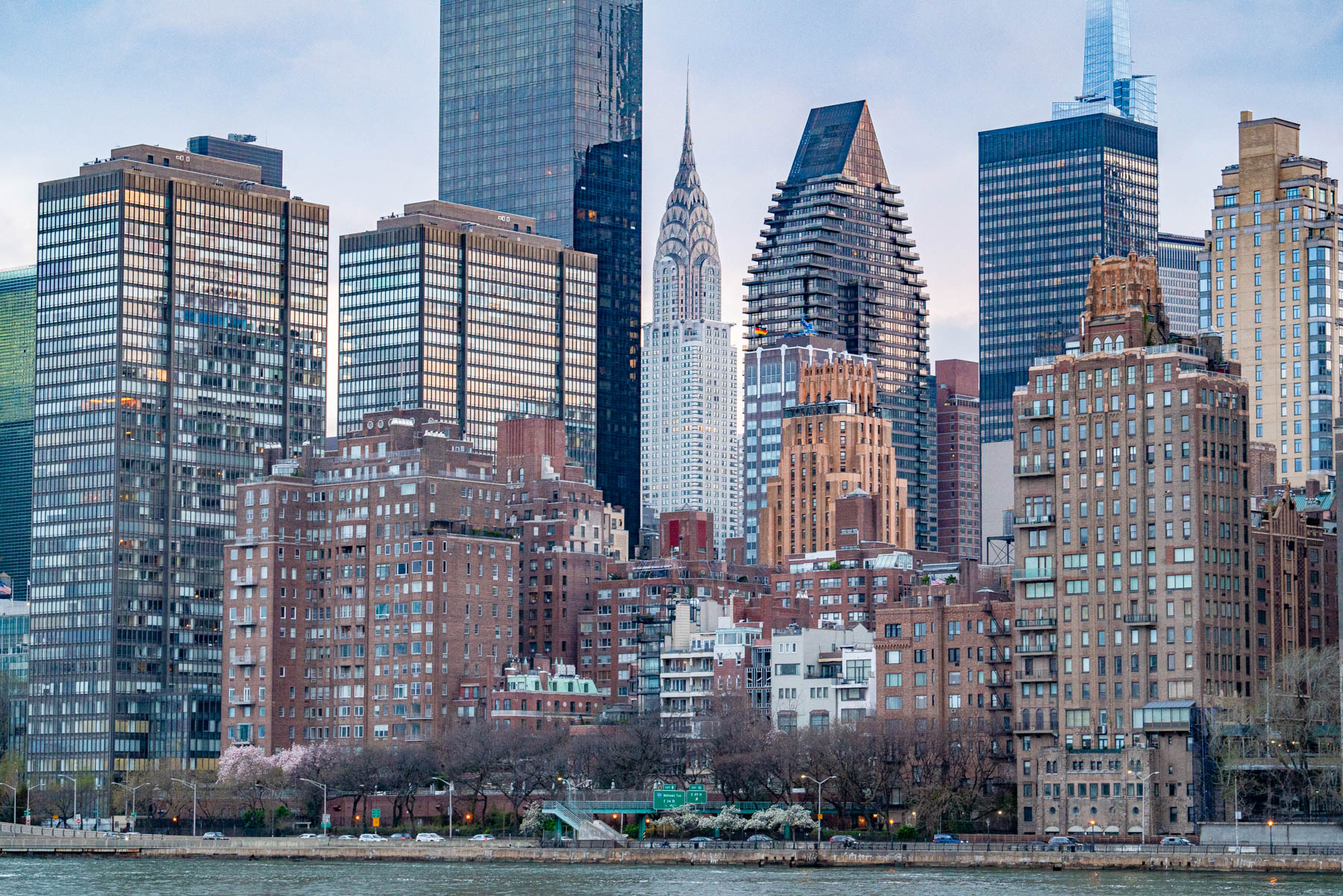 The Manhattan skyline with the Chrysler Building rises above the East River at dusk.