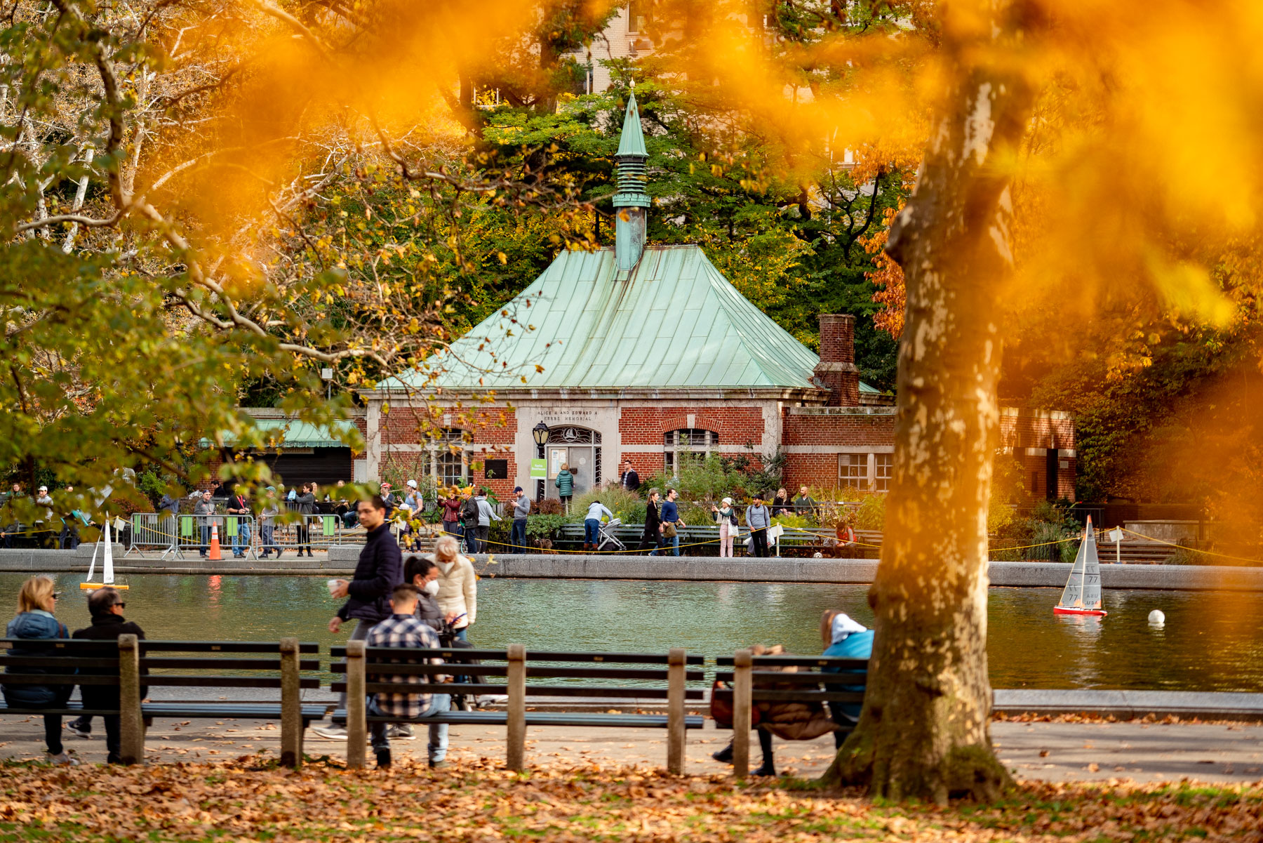 People gather around the model boat pond near the Kerbs Boathouse in Central Park during fall foliage.