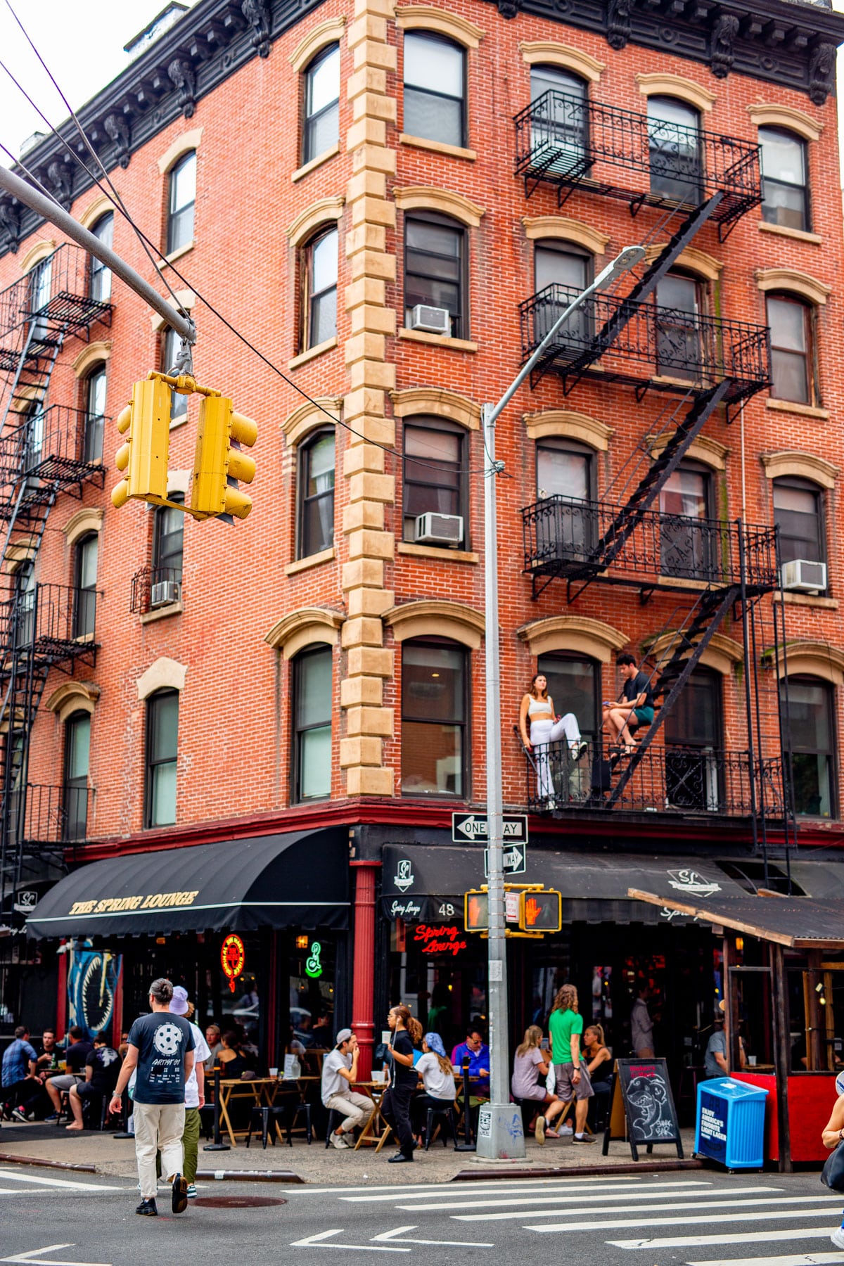 A red brick building with fire escapes and ground-floor bars sits on a Soho street corner.