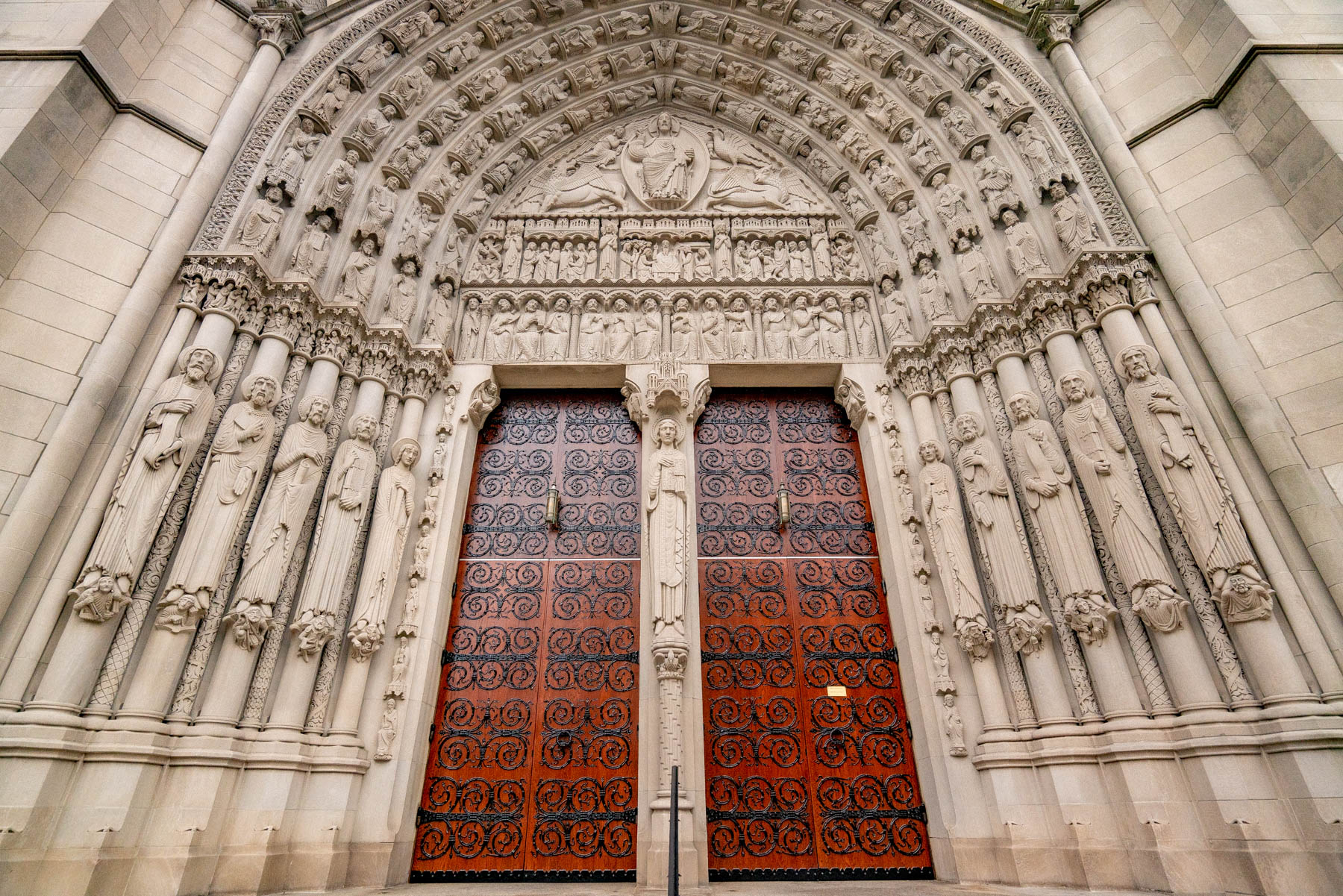 Ornate carved stone portal with bronze doors at a Gothic cathedral entrance.