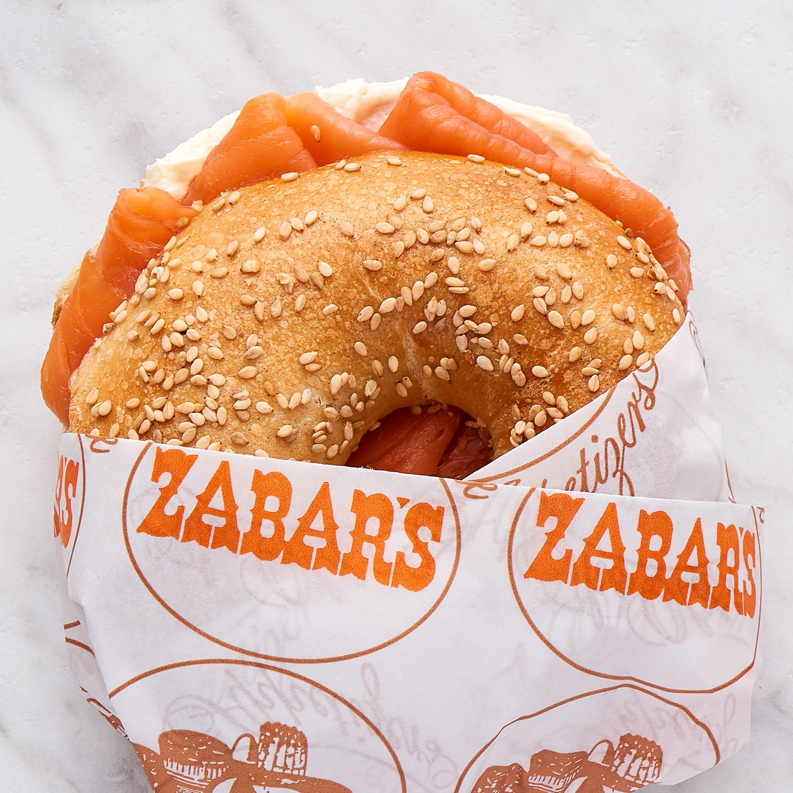 A sesame bagel with cream cheese and lox is wrapped in Zabar's paper.