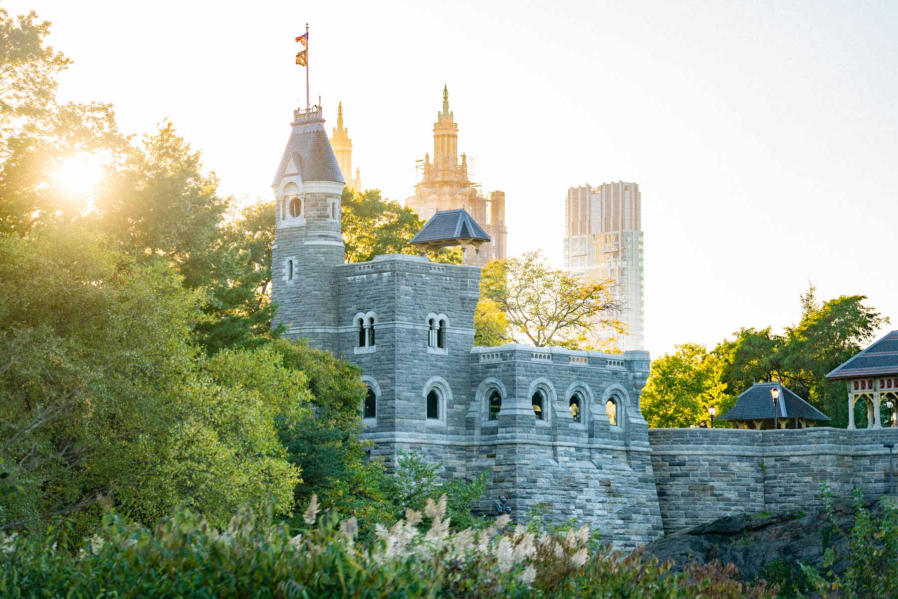Belvedere Castle rises above trees in Central Park at sunrise with city towers behind it.