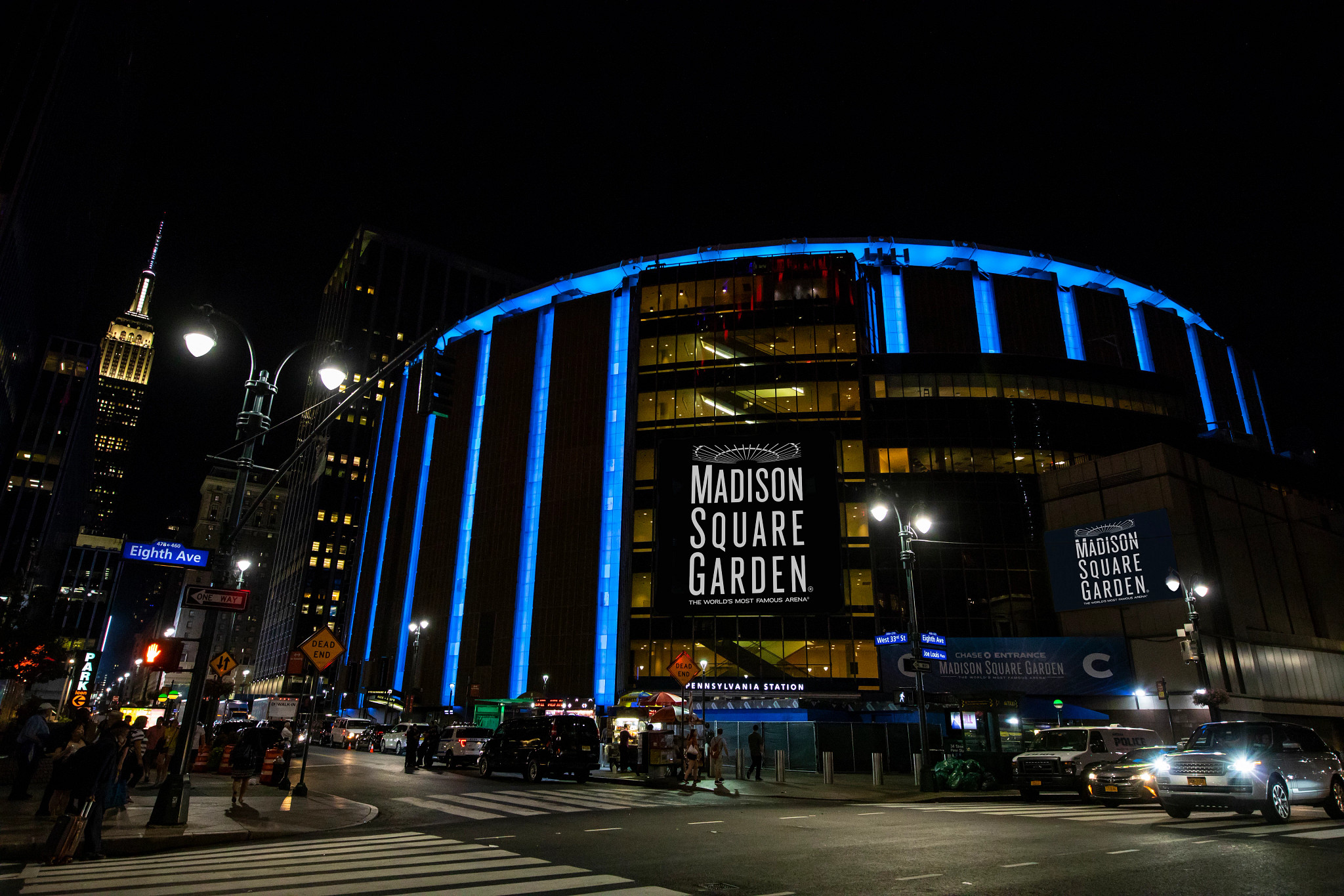 Madison Square Garden is lit blue at night with the Empire State Building visible in the distance.
