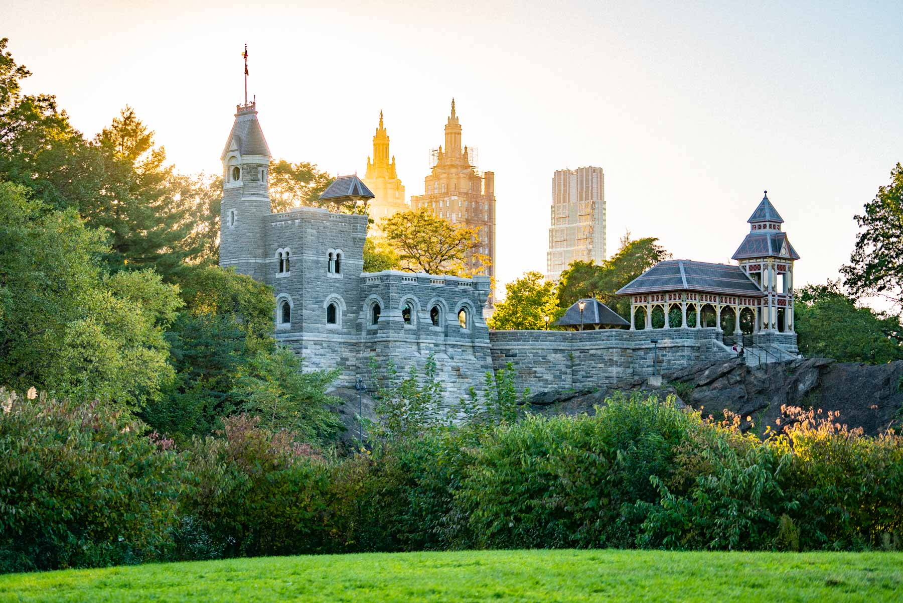 Belvedere Castle rises above Central Park's trees with skyline towers behind it at sunrise.