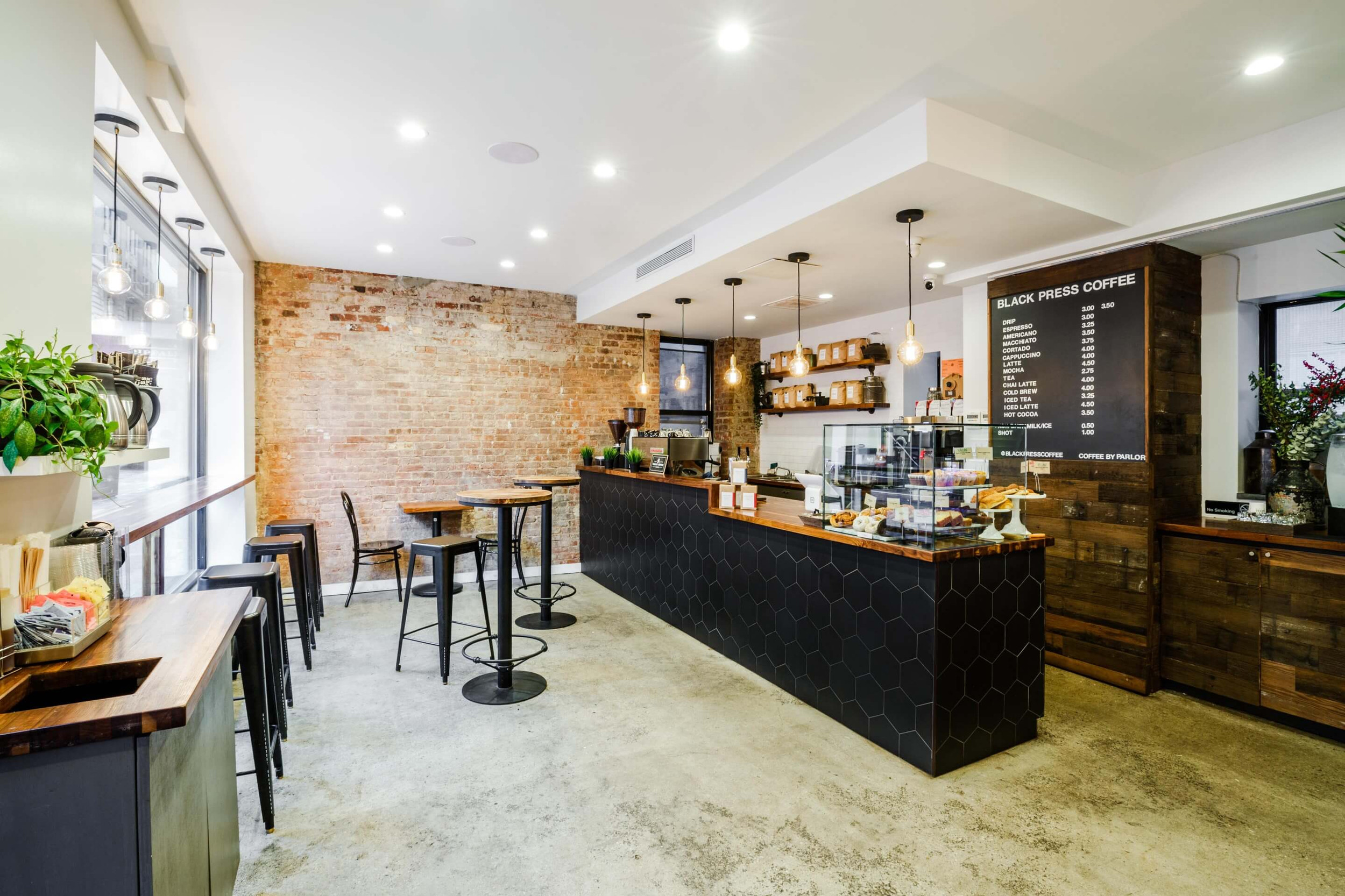 An empty coffee shop interior with a black tiled counter and exposed brick wall.