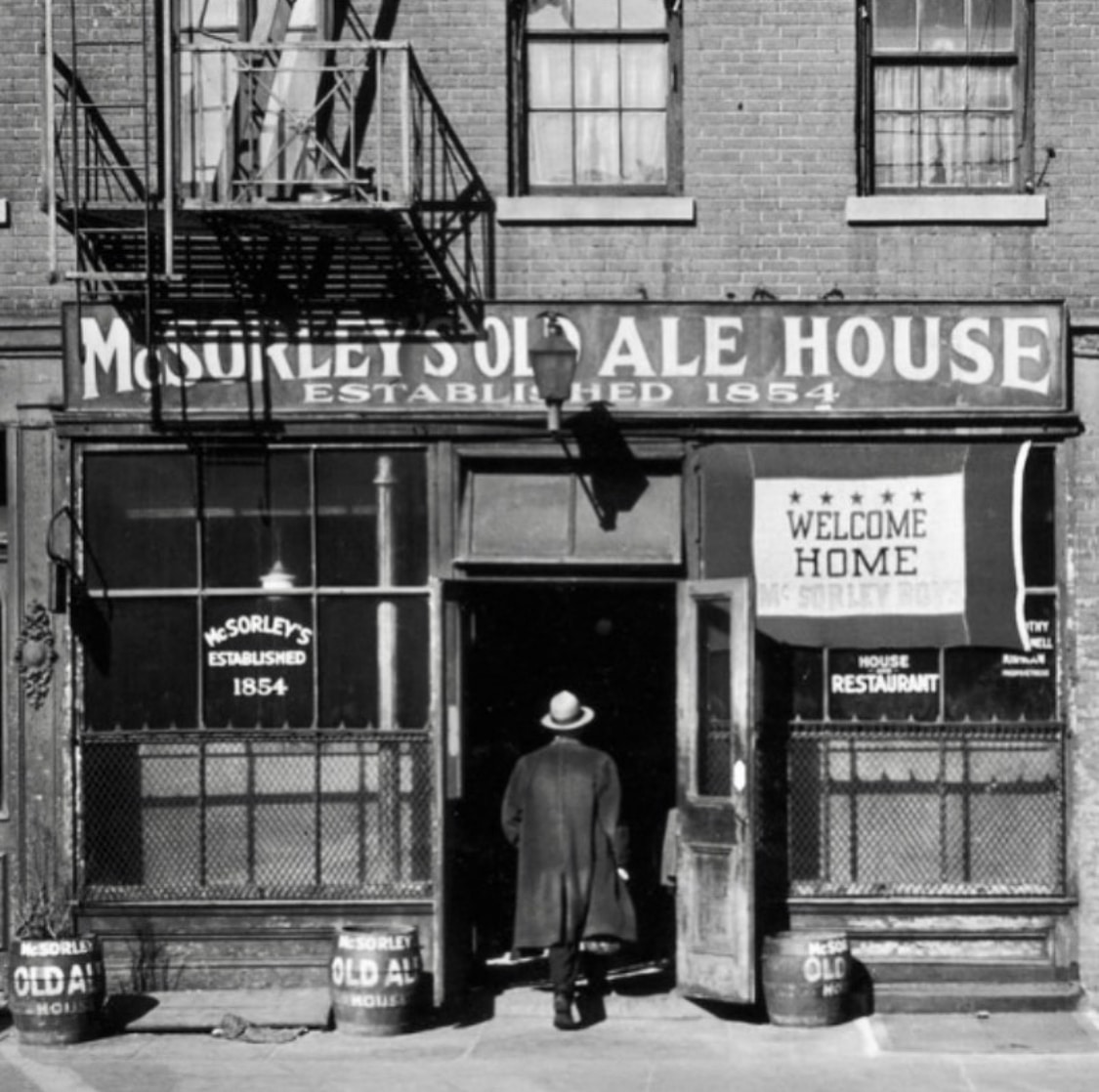 A man in a coat and hat enters McSorley's Old Ale House through its storefront door.