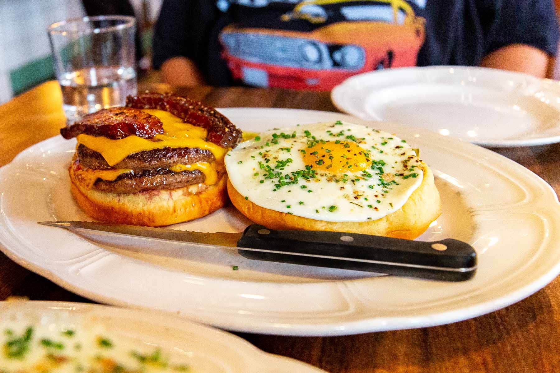 A double cheeseburger with bacon and a fried egg is served open-faced on a plate.