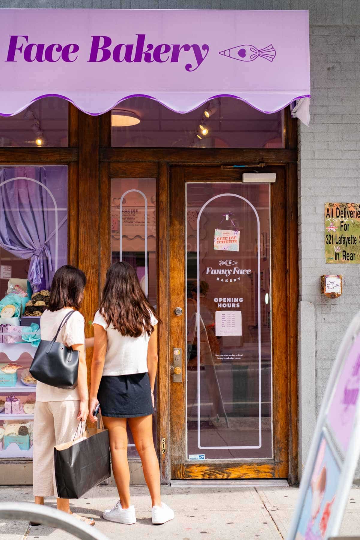 Two women look into the window display of Funny Face Bakery from the sidewalk.