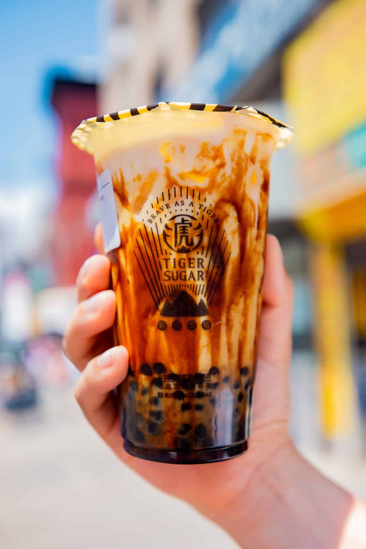 A brown sugar boba milk tea with caramel streaks running down the inside of the clear cup, held in hand