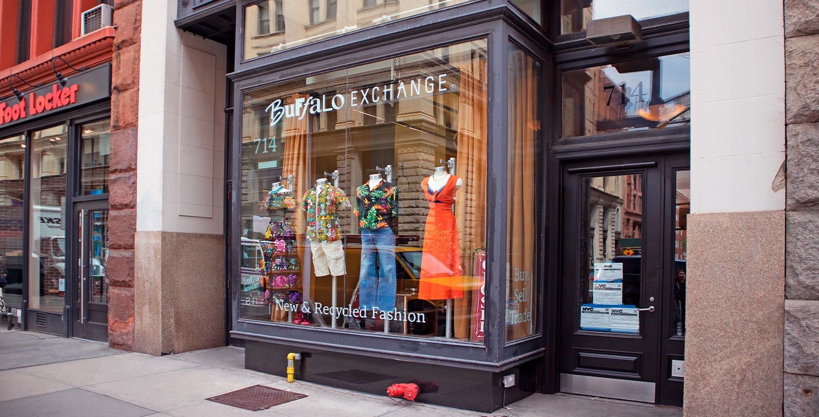 A Buffalo Exchange storefront with mannequins in the window on a city street.