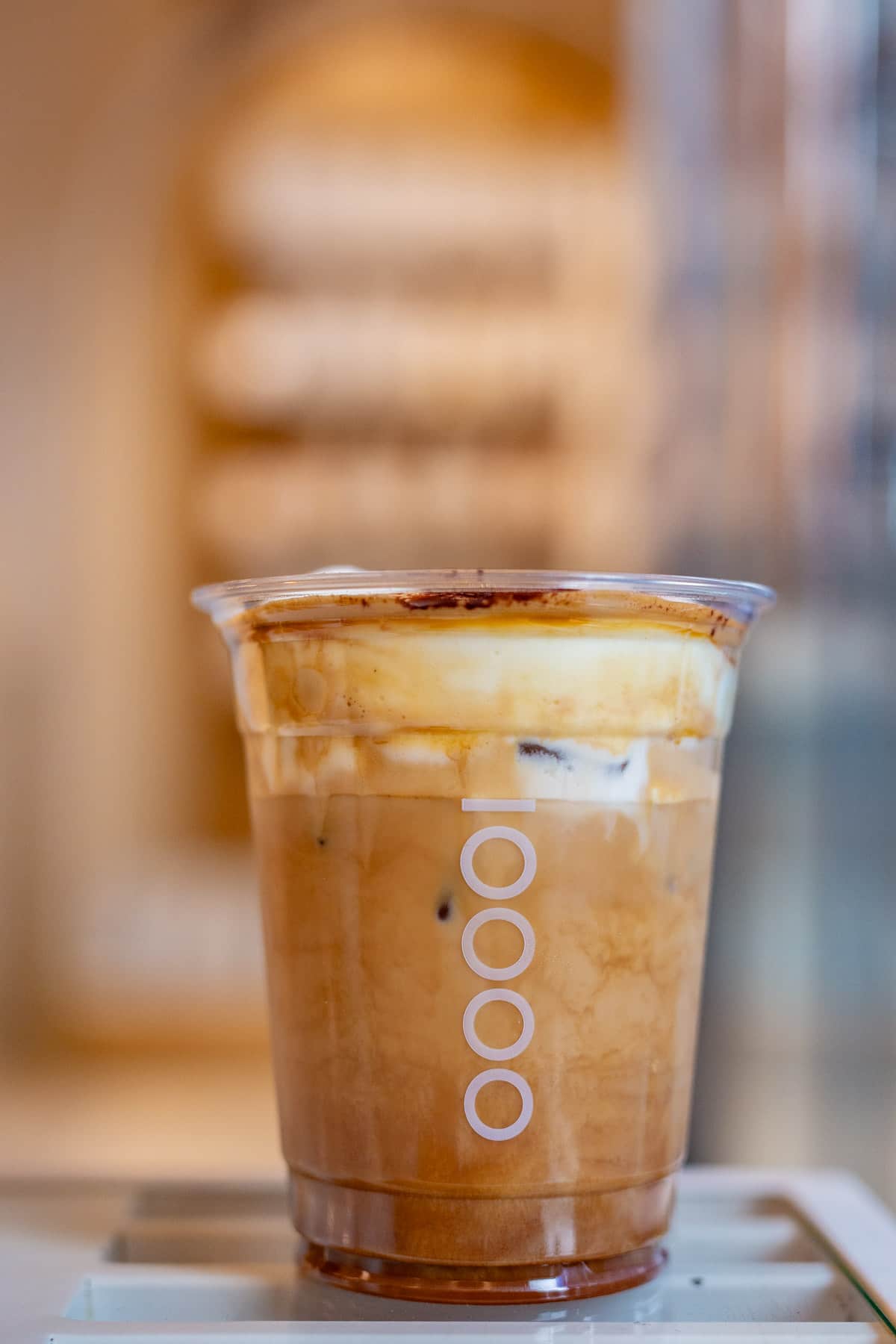 An iced coffee drink in a plastic cup with a logo of ten circles sits on a table.