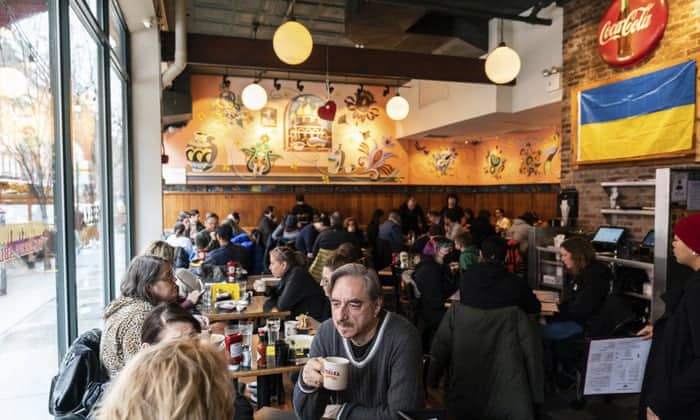 Diners fill the tables at a busy Ukrainian diner with a large Ukrainian flag on the wall.