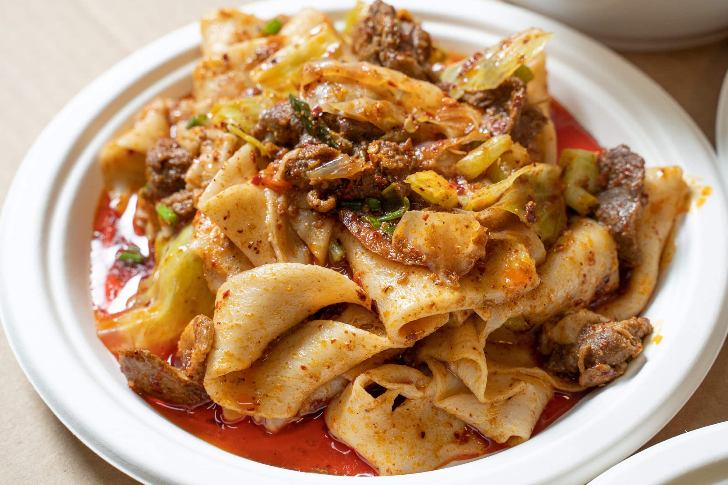 Close-up of hand-pulled Chinese noodles with cabbage and chunks of meat in a pool of chili oil