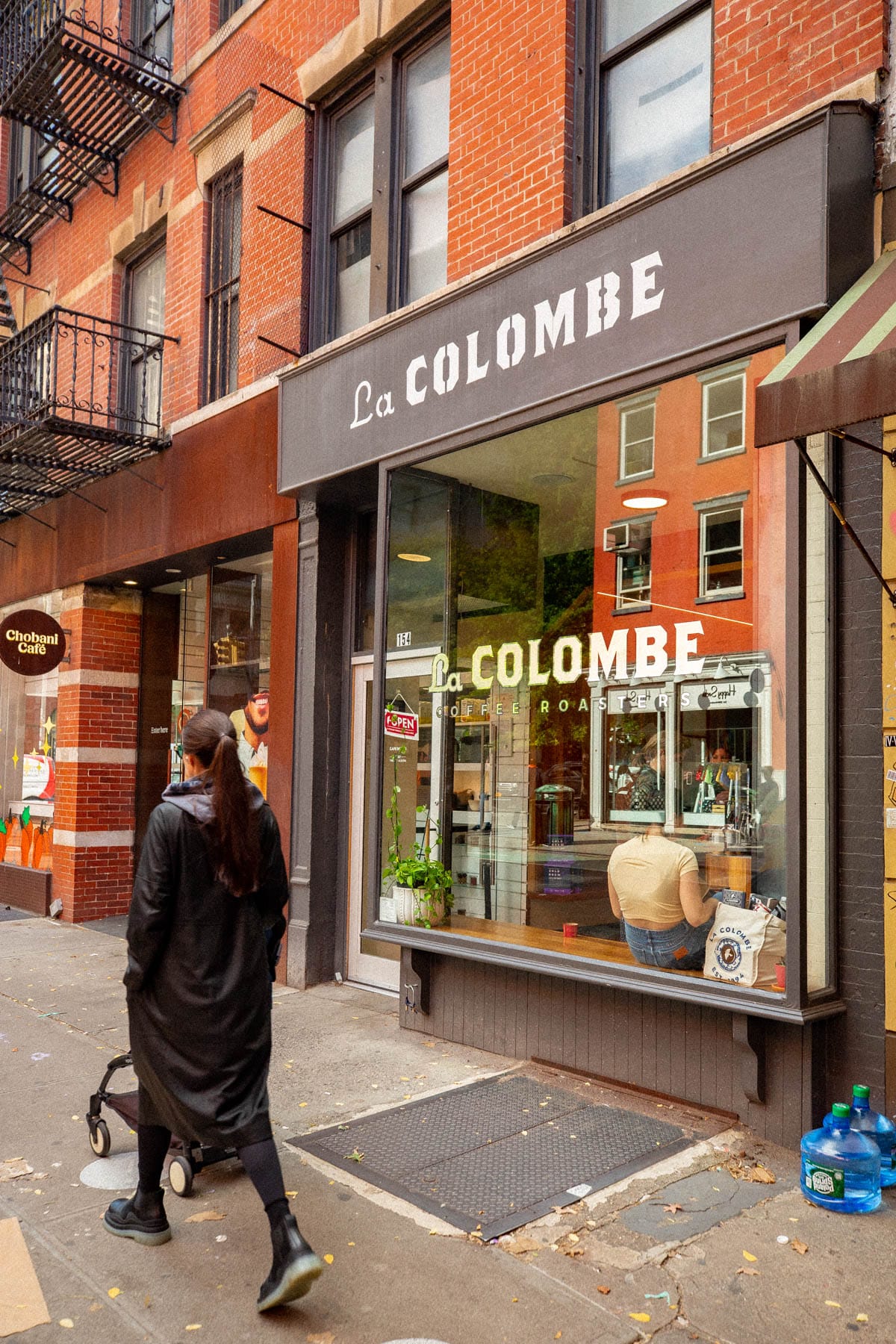 A pedestrian walks past the storefront of La Colombe Coffee Roasters on a brick-lined street.