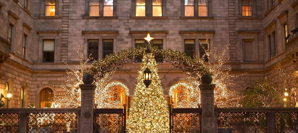 A lit Christmas tree stands in the courtyard entrance of the Lotte New York Palace hotel at night.
