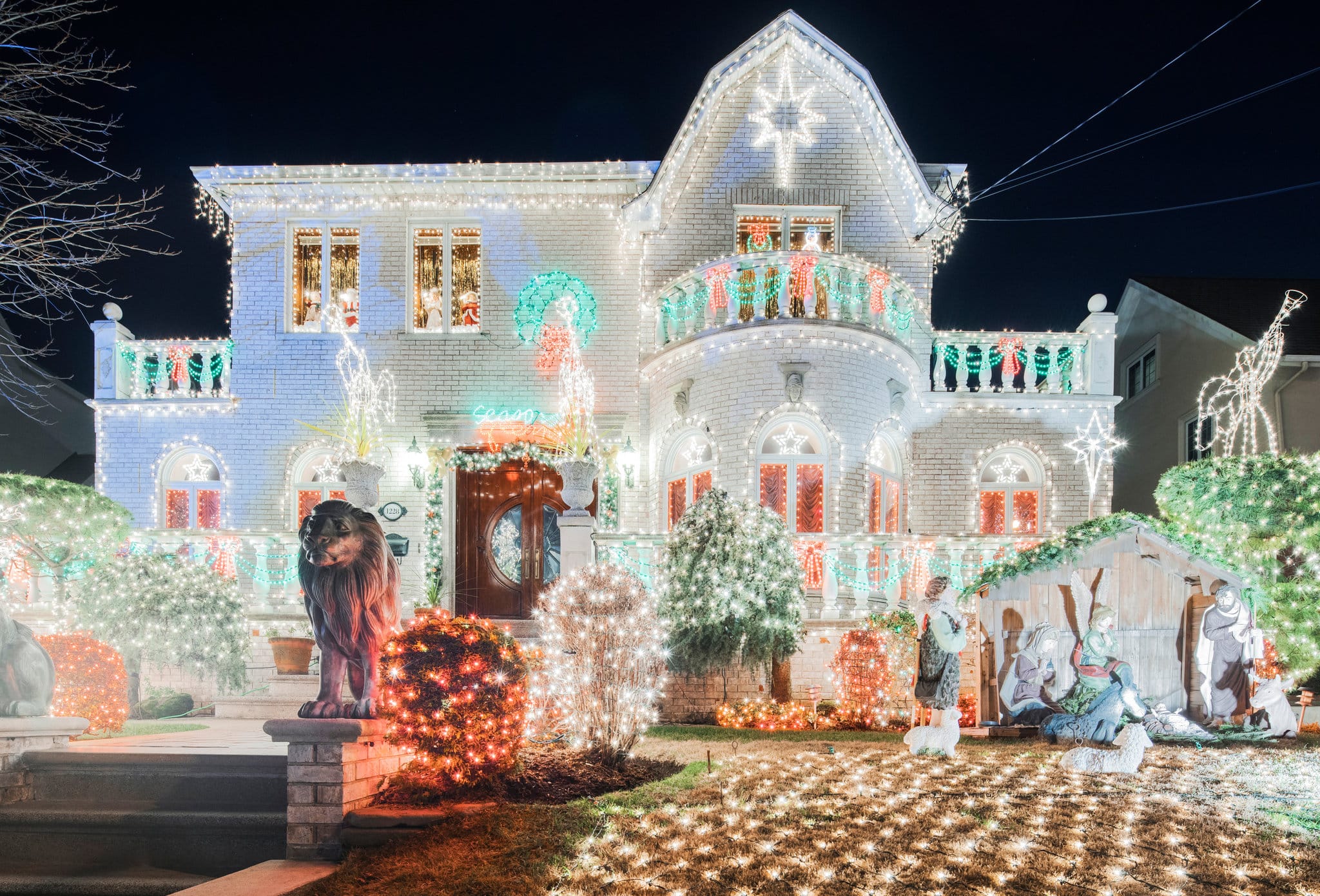 A house elaborately decorated with Christmas lights, statues, and a nativity scene at night.