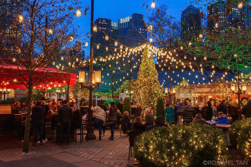Crowds gather in the outdoor garden at Tavern on the Green decorated with Christmas lights at dusk.