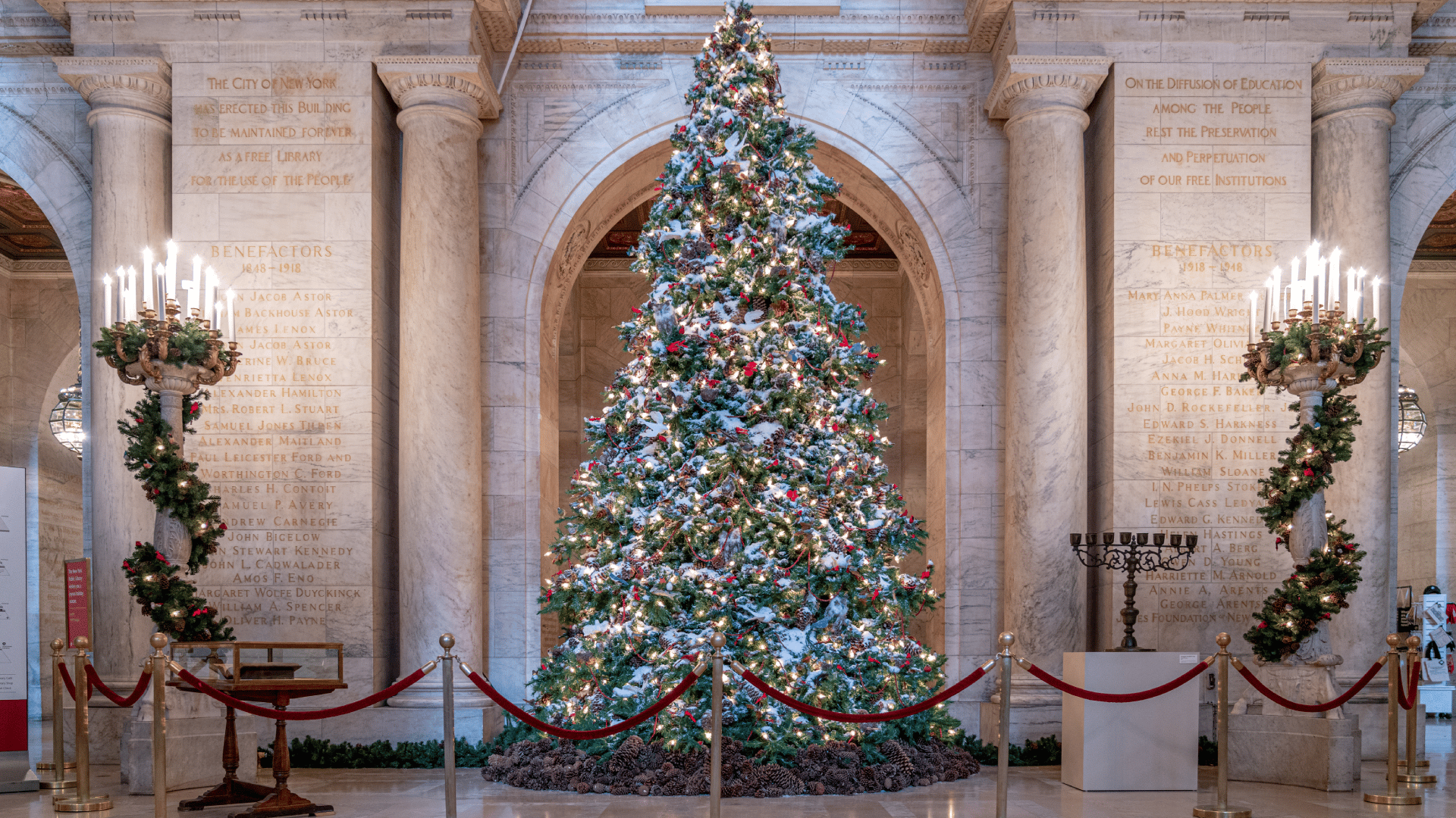 A large decorated Christmas tree stands in a marble hall lined with columns and engraved donor names.