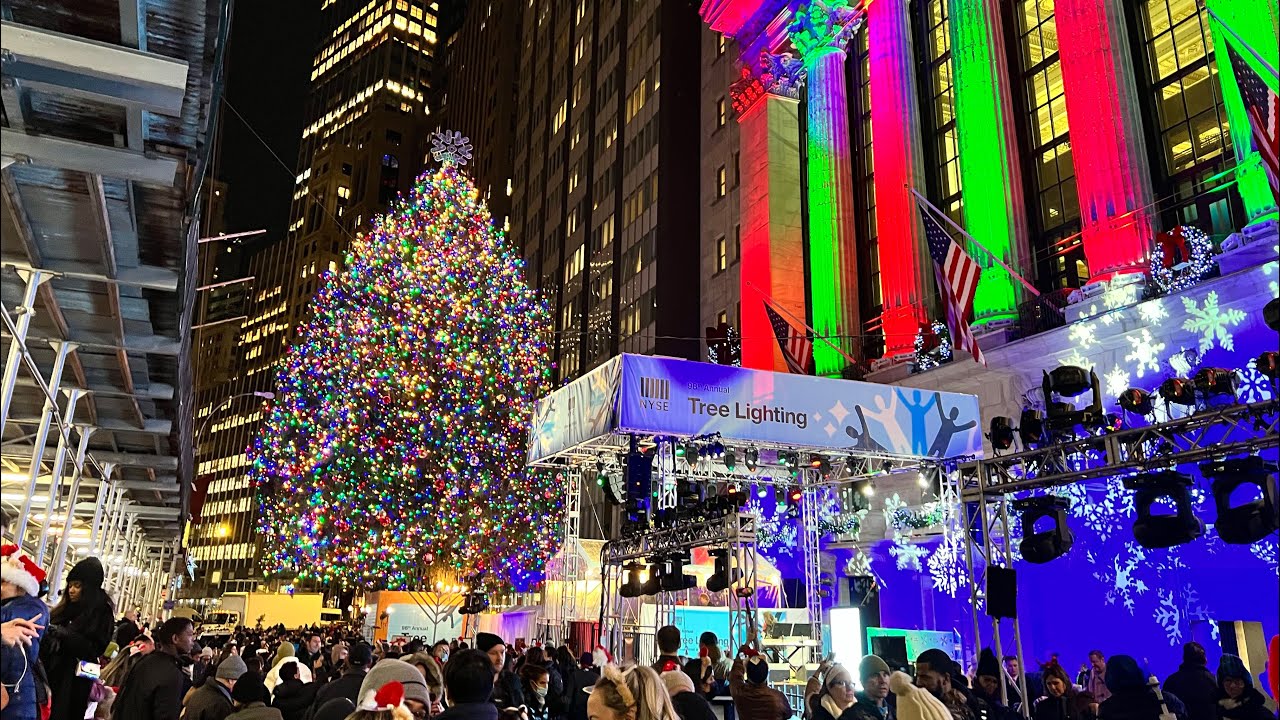 A crowd gathers at night for a Christmas tree lighting outside the New York Stock Exchange decorated with colored lights.