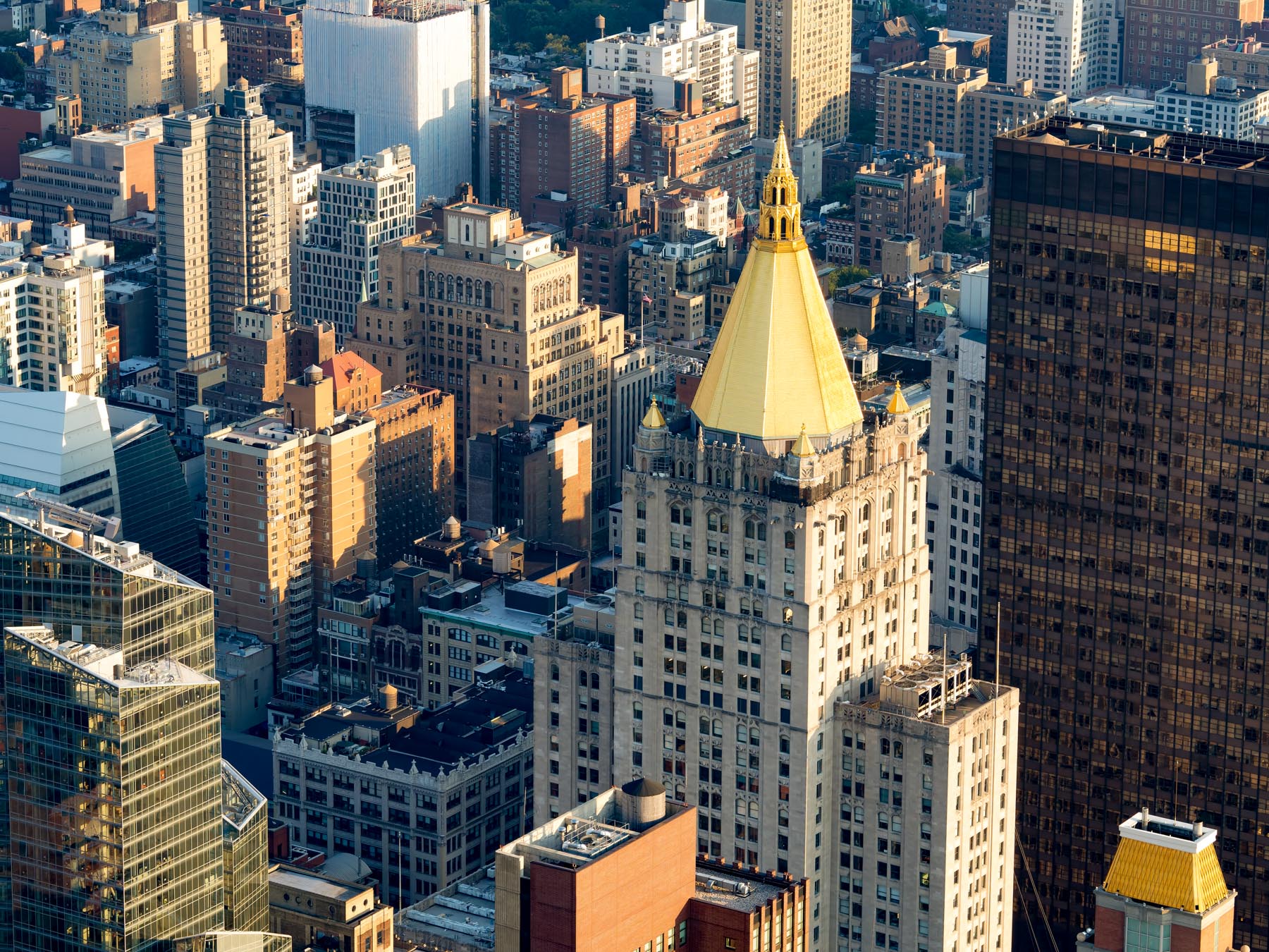 An aerial view of Midtown Manhattan rooftops with the golden-topped New York Life Building at center.