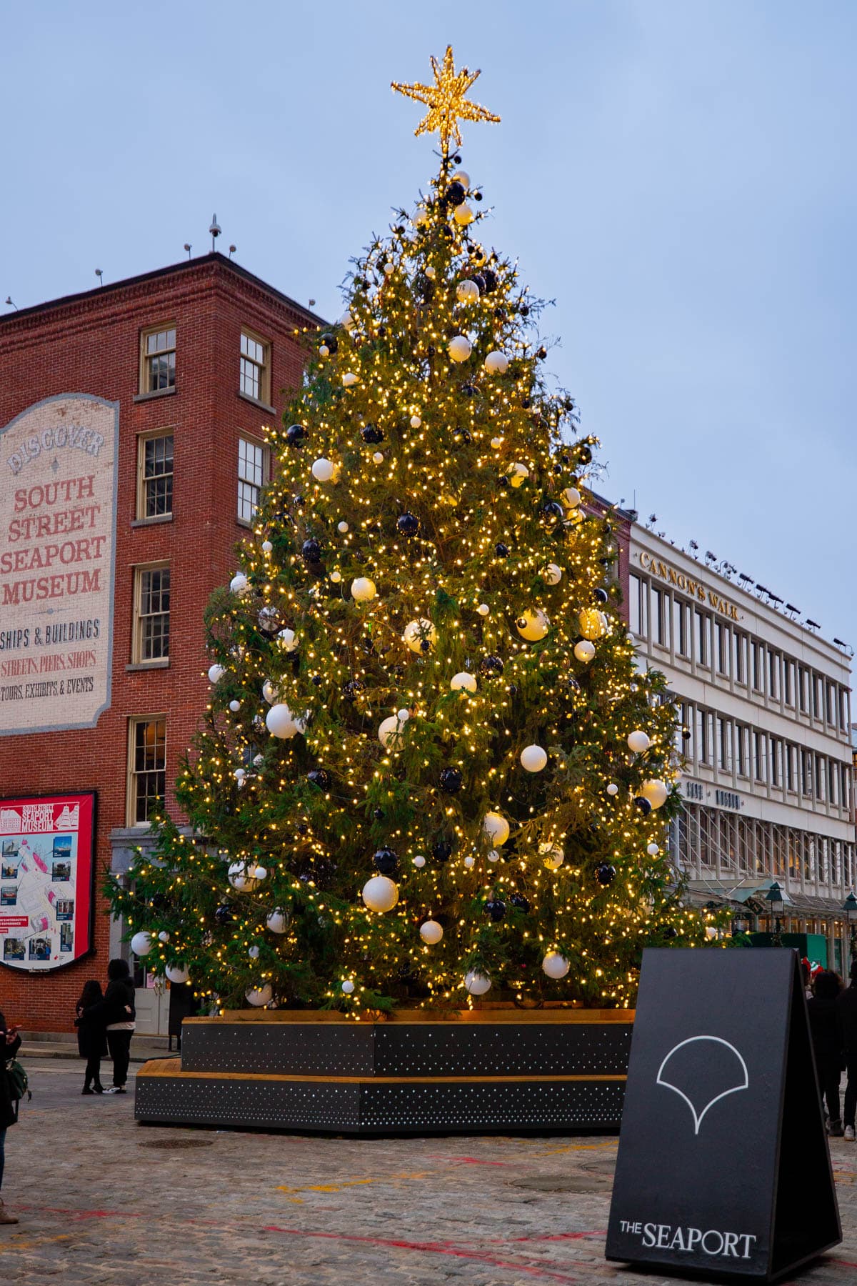 A large decorated Christmas tree stands in the cobblestone plaza at South Street Seaport.