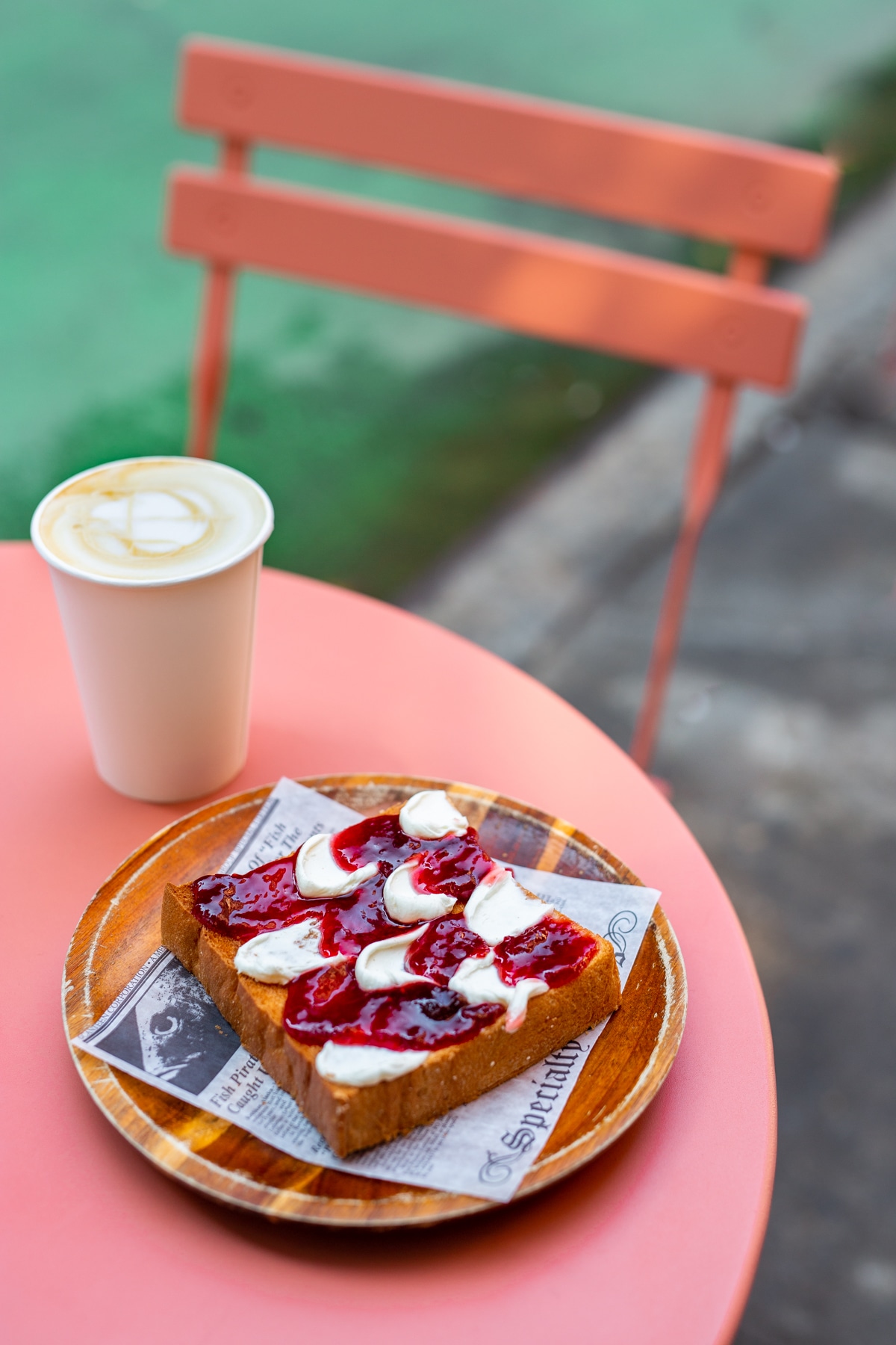 Berry toast with a latte sit on a pink café table beside a matching chair.