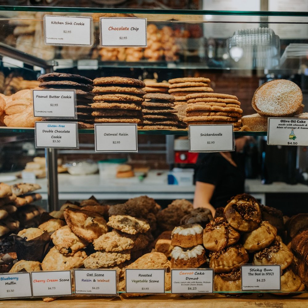 A bakery display case filled with cookies, scones, and pastries with price signs.