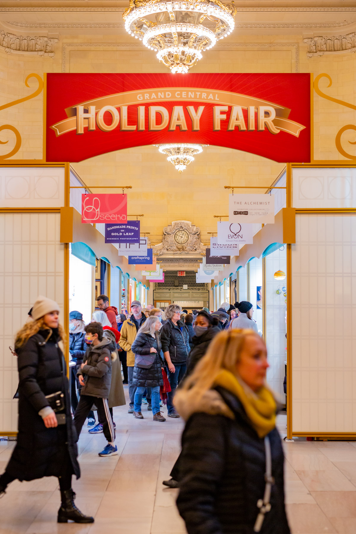 Shoppers pass through the entrance of the Grand Central Holiday Fair under a red banner.