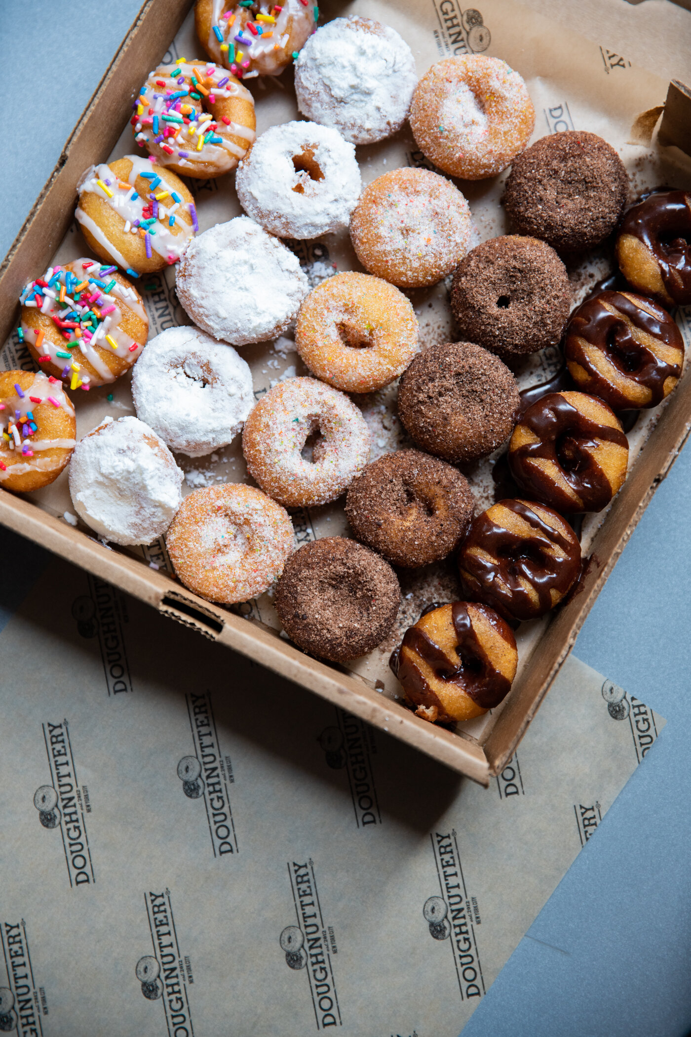 A box of assorted mini doughnuts from Doughnuttery sits on branded paper.