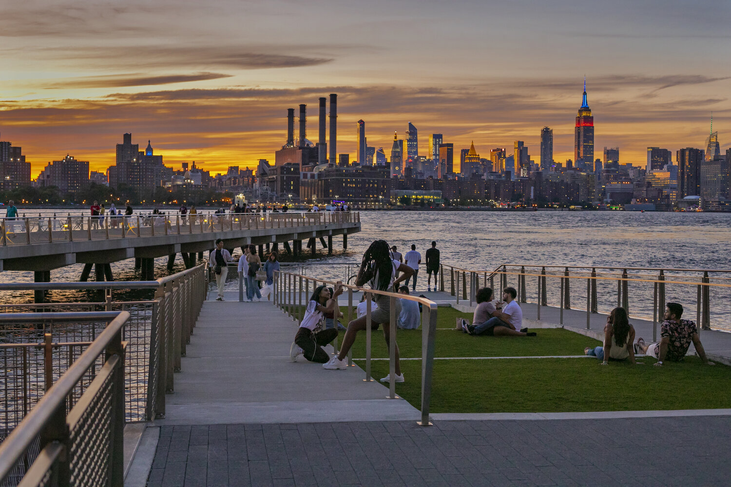 People gather on piers at a Williamsburg waterfront park watching the Manhattan skyline at sunset.