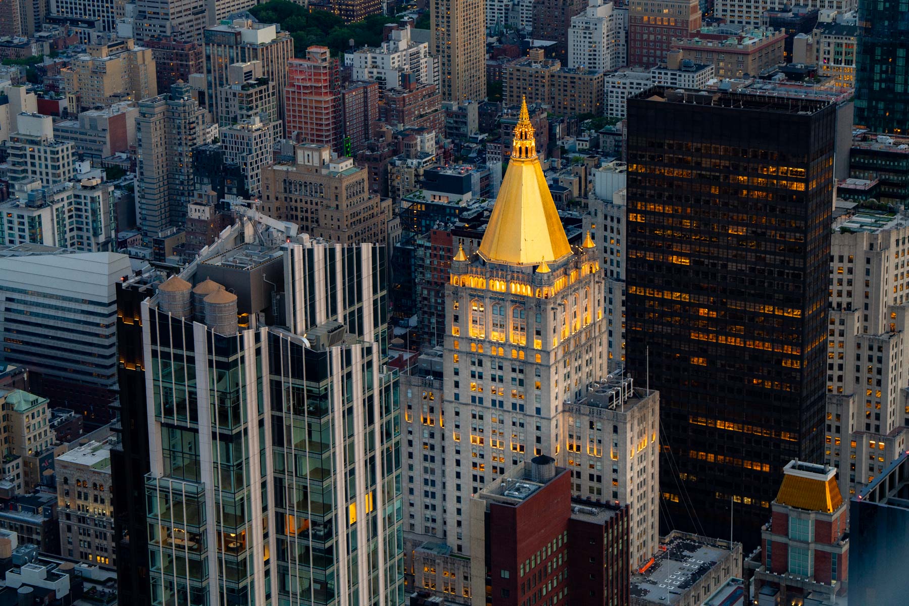 An aerial view of Manhattan skyscrapers at dusk with a golden-topped tower illuminated among them.