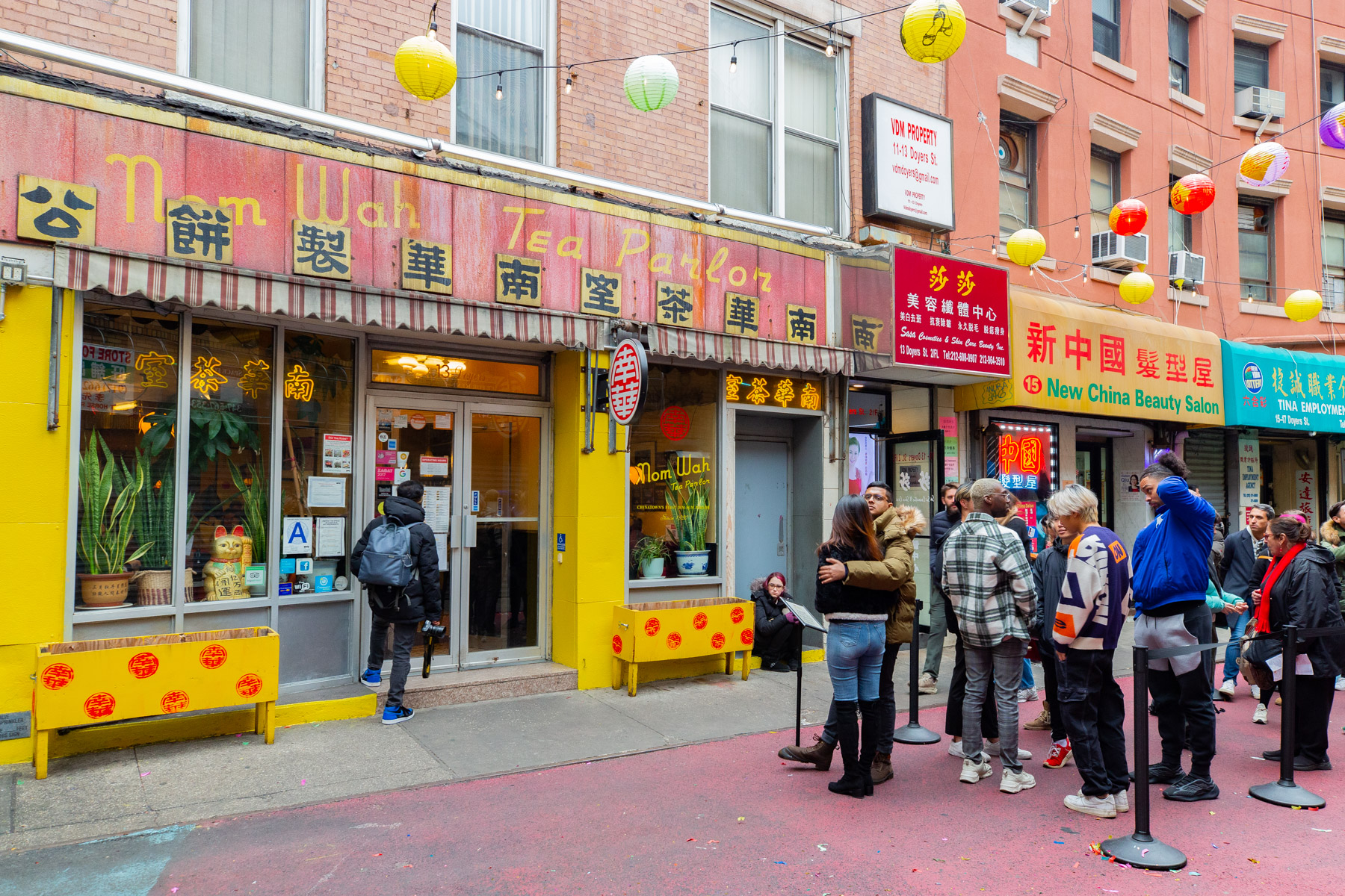 People gather on a Chinatown street lined with lanterns near Nom Wah Tea Parlor during a Lunar New Year celebration.