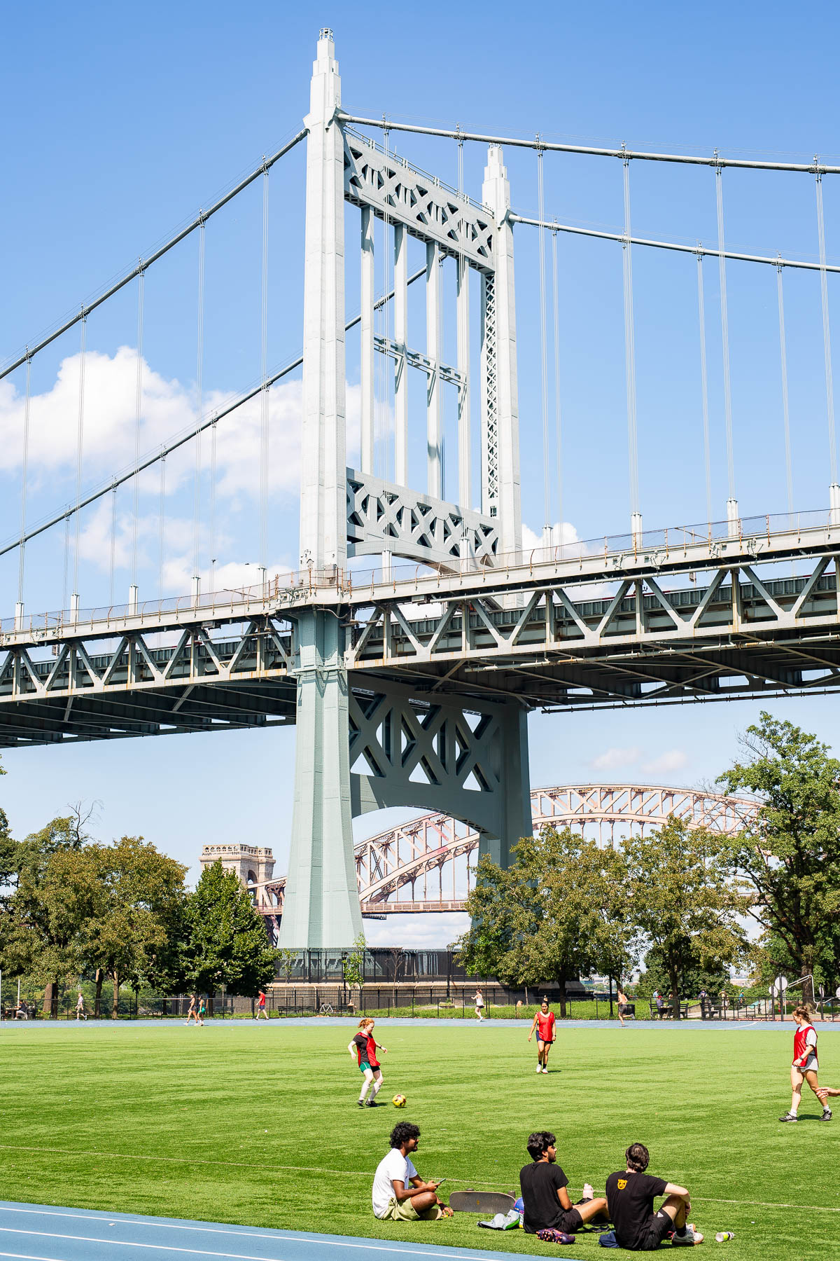 People play soccer and sit on a field beneath the Triborough (RFK) Bridge tower at Astoria Park.