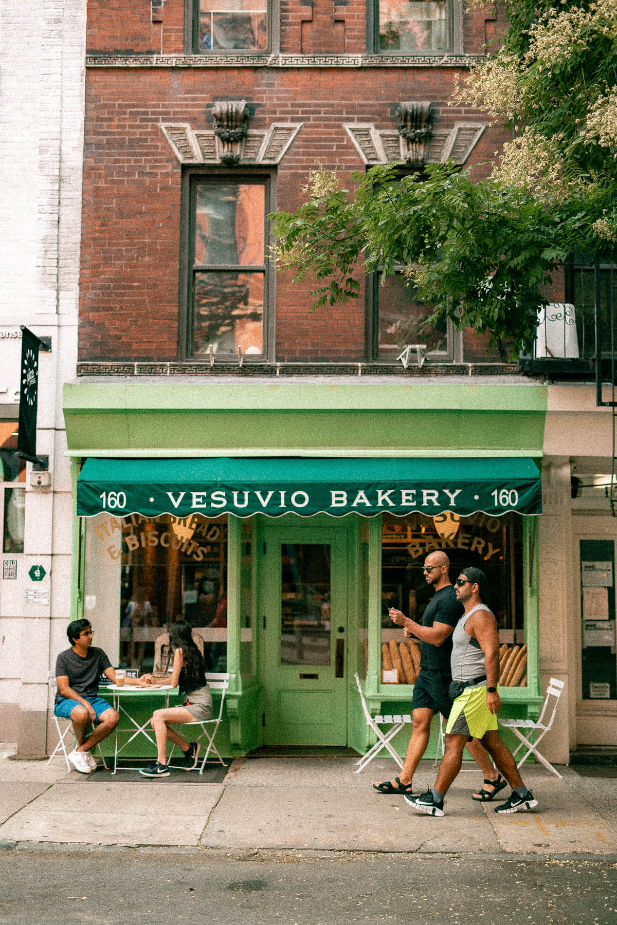 couple enjoying a cup of coffee at Vesuvio Bakery in SoHo in NYC, people on a walk passing Vesuvio Bakery