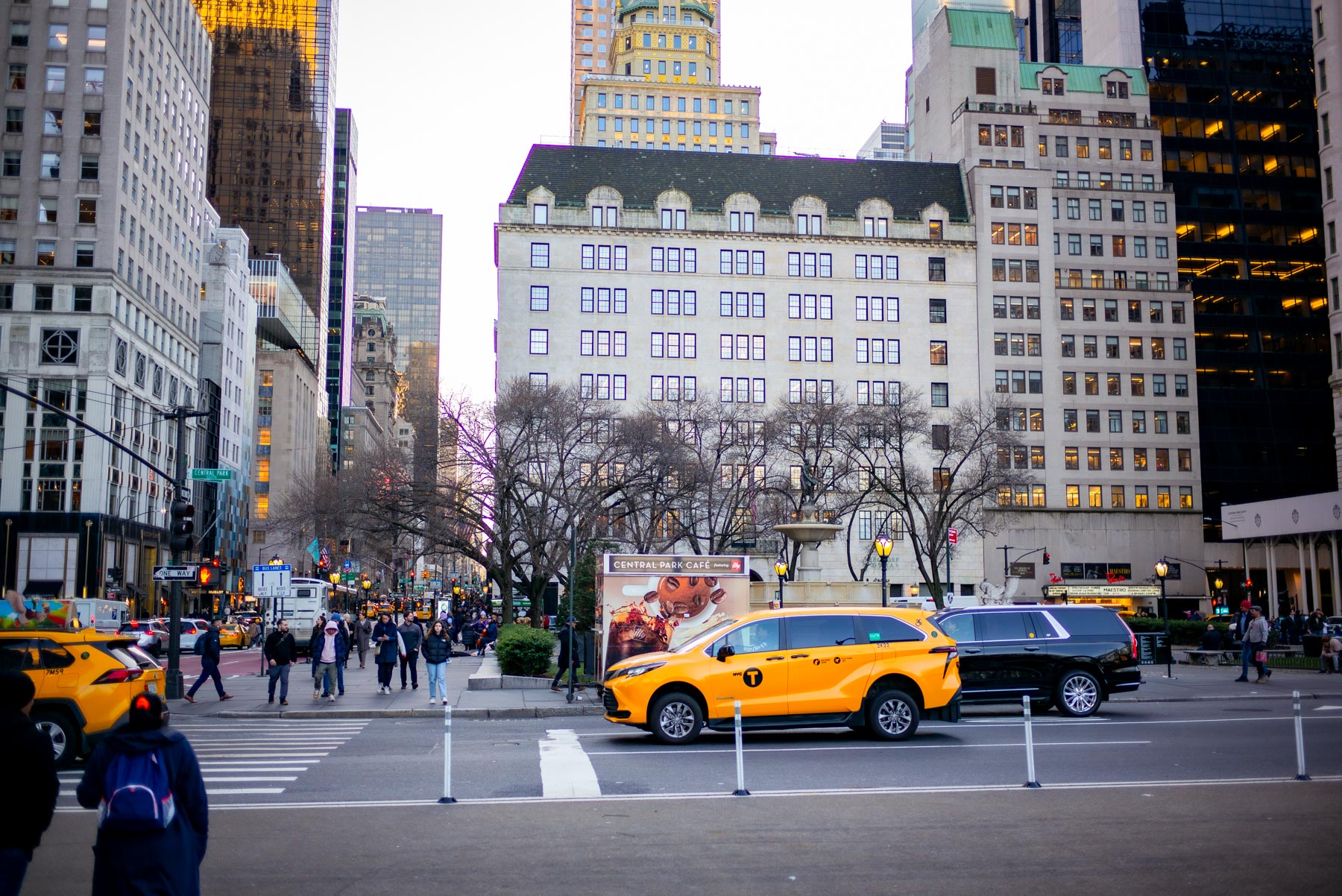 Taxis and pedestrians cross a busy Fifth Avenue intersection near the Plaza Hotel.