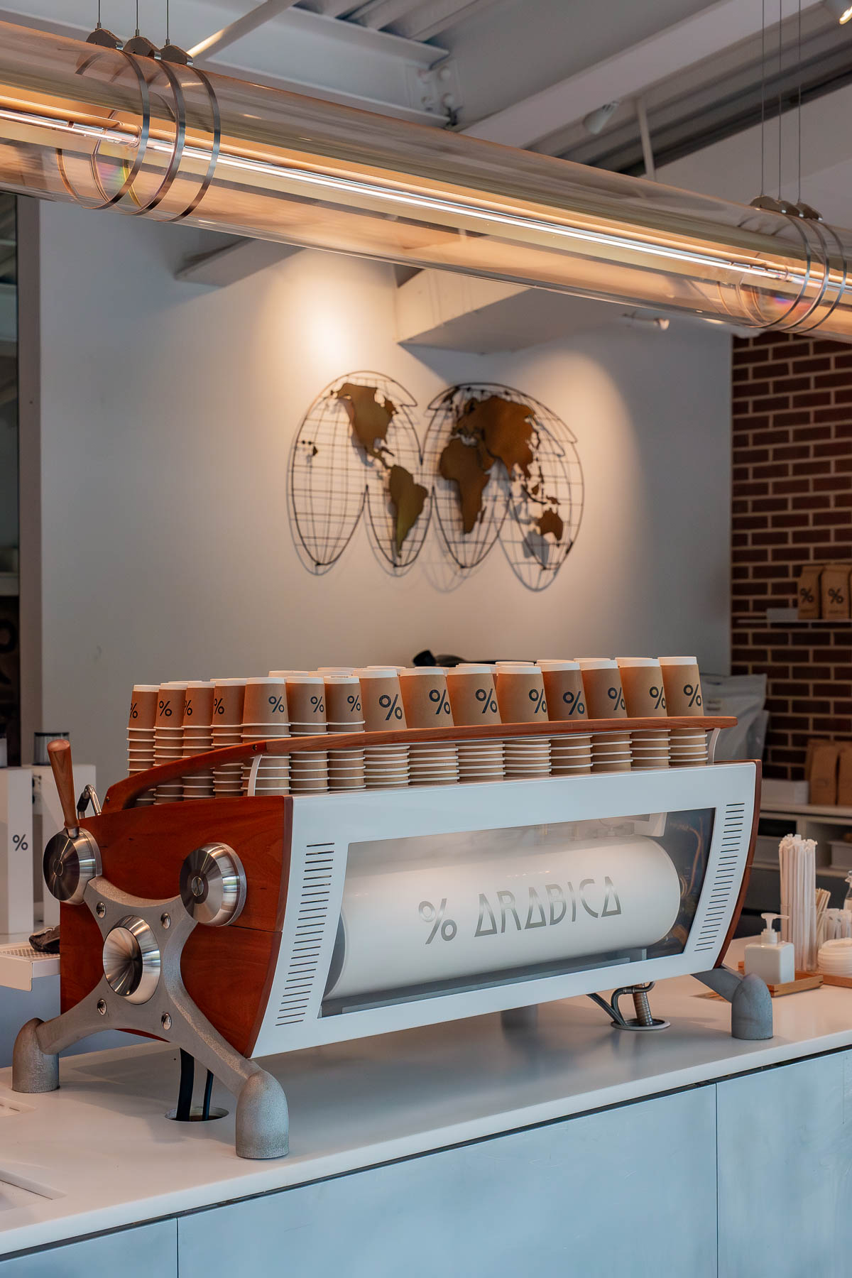 An espresso machine with stacked cups sits on the counter at % Arabica in DUMBO.