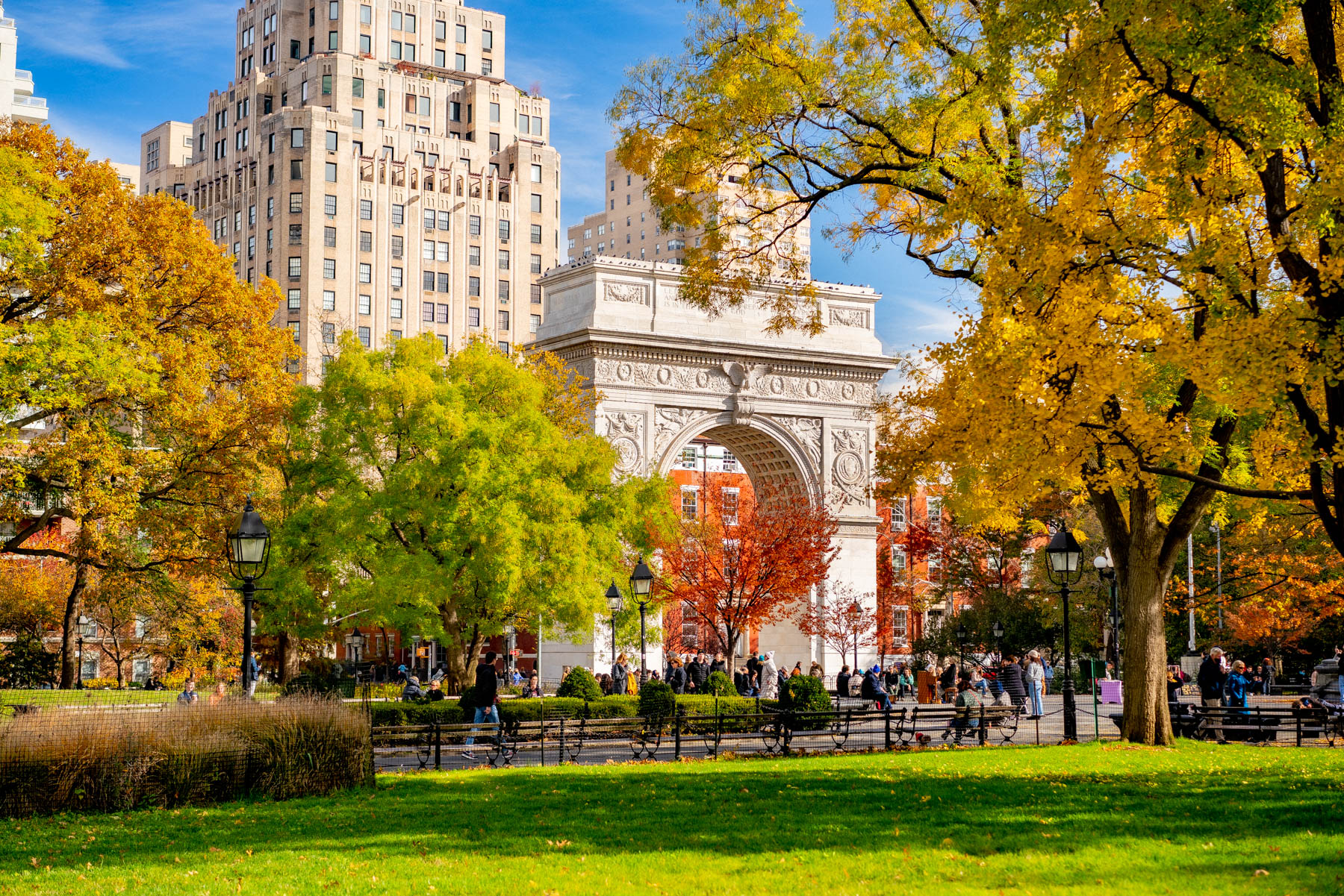 Washington Square Arch stands framed by fall foliage with a highrise behind it.