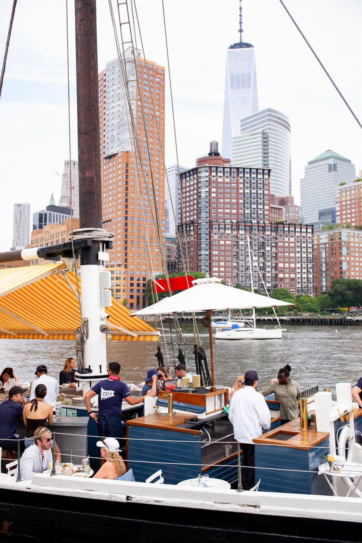People gather aboard the Grand Banks boat bar on the Hudson River with the Lower Manhattan skyline behind.