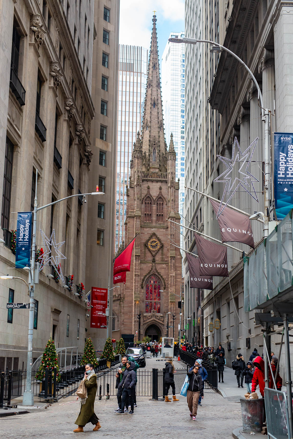 Trinity Church spire rises above a Wall Street street decorated with holiday banners and stars