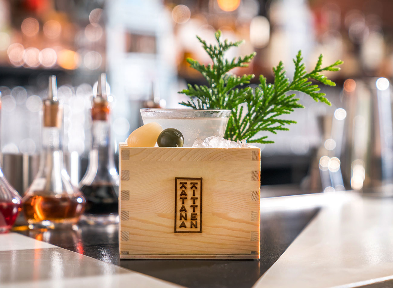 A cocktail served in a wooden box branded Katana Kitten sits on a bar.