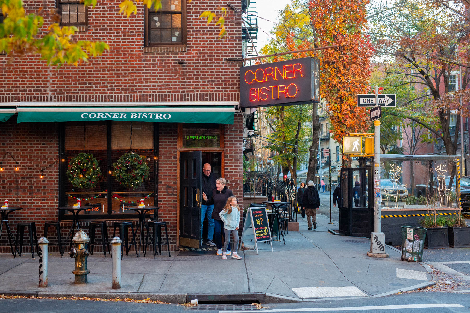 A family exits Corner Bistro on a West Village street corner in fall.