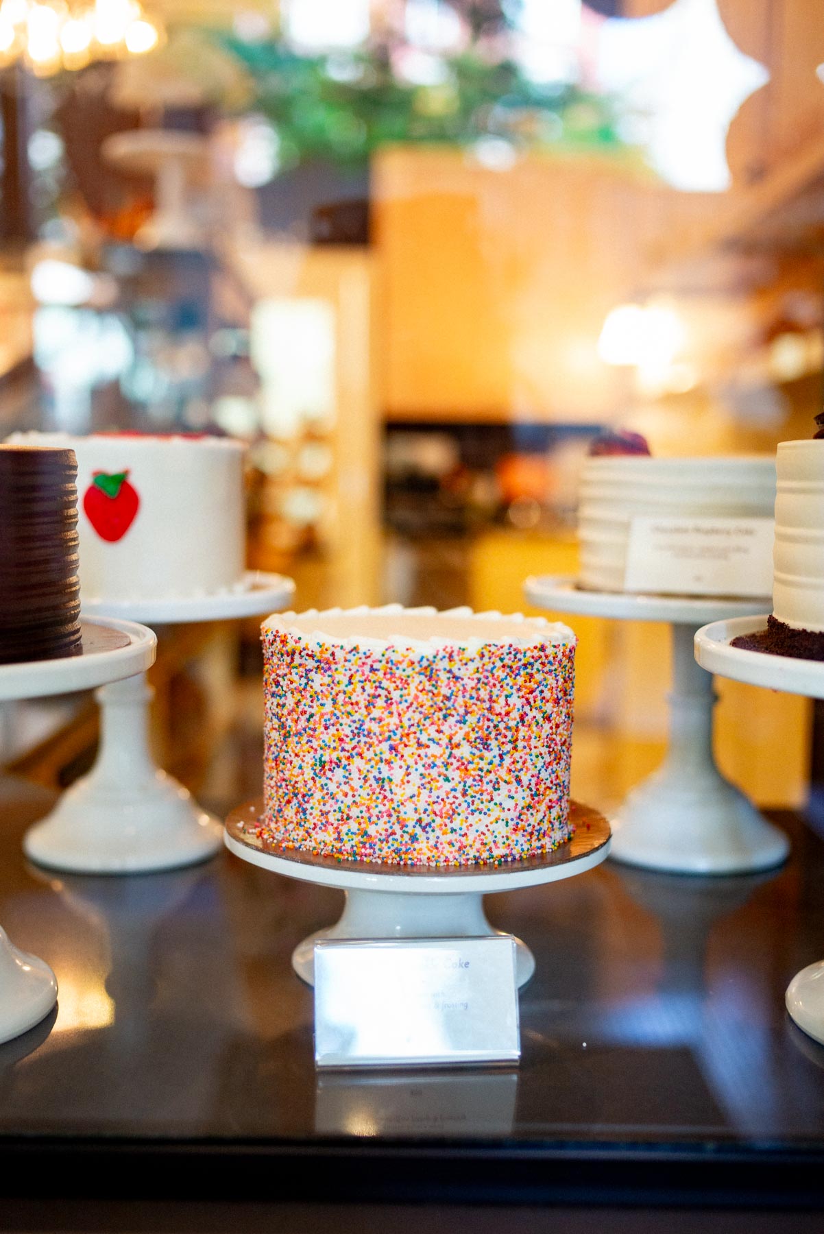 Cakes displayed on stands in a bakery case, including a sprinkle-covered cake.