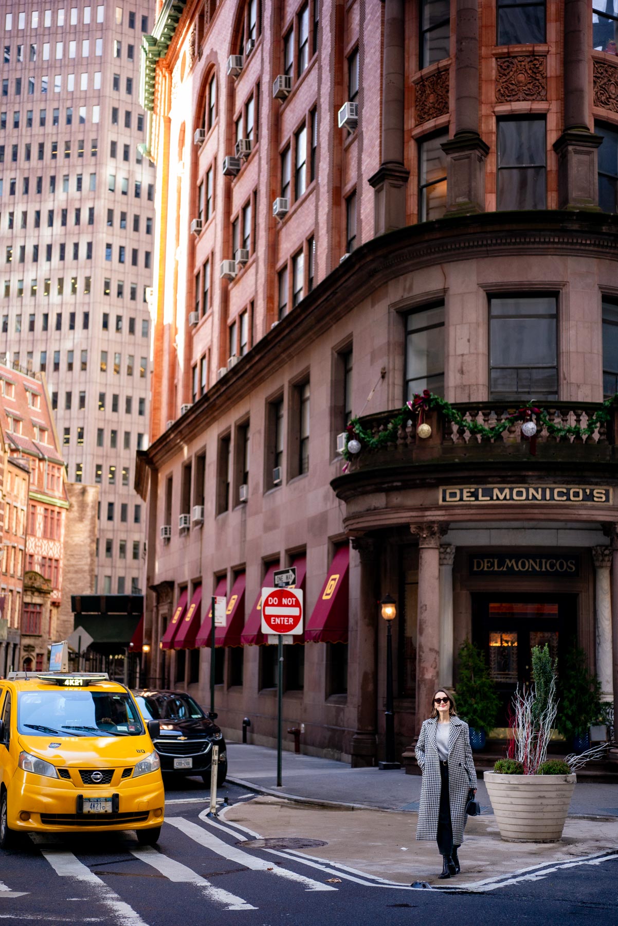 A woman crosses the street near the Delmonico's building on a Financial District corner with a taxi passing by.